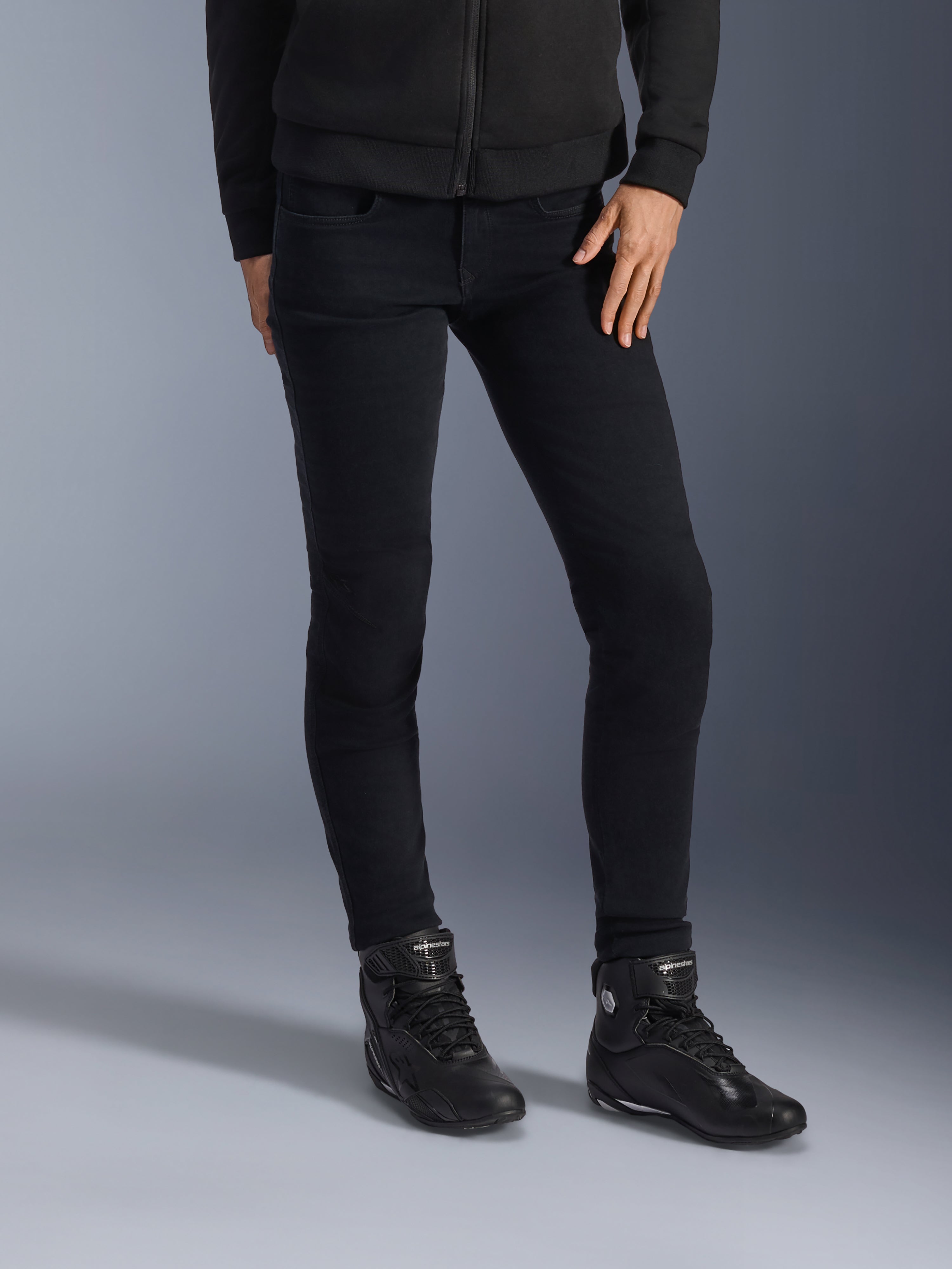 Alpinestars Daisy V3 dames motorjeans, Rinse Black, slim-fit motorbroek, gecombineerd met zwarte hoge motorschoenen en een hoodie met ritssluiting, strakke monochrome urban styling