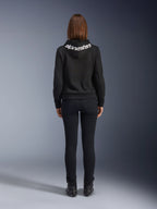 Alpinestars Daisy V3 dames motorjeans, Black Rinse, slim fit motorbroek, achteraanzicht met hoge taille en vrouwelijk silhouet, gecombineerd met een zwarte Alpinestars hoodie en zwarte motorlaarzen, urban casual motorkleding