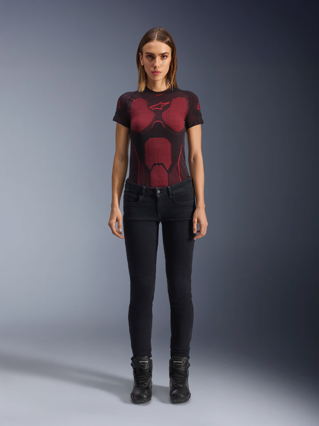Alpinestars Daisy V3 dames motorjeans, Rinse Black, slim-fit motorbroek, gedragen door een model met een rood en zwart technisch T-shirt en zwarte motorlaarzen, casual urban motoruitrusting met een vrouwelijk silhouet en high-waisted ontwerp