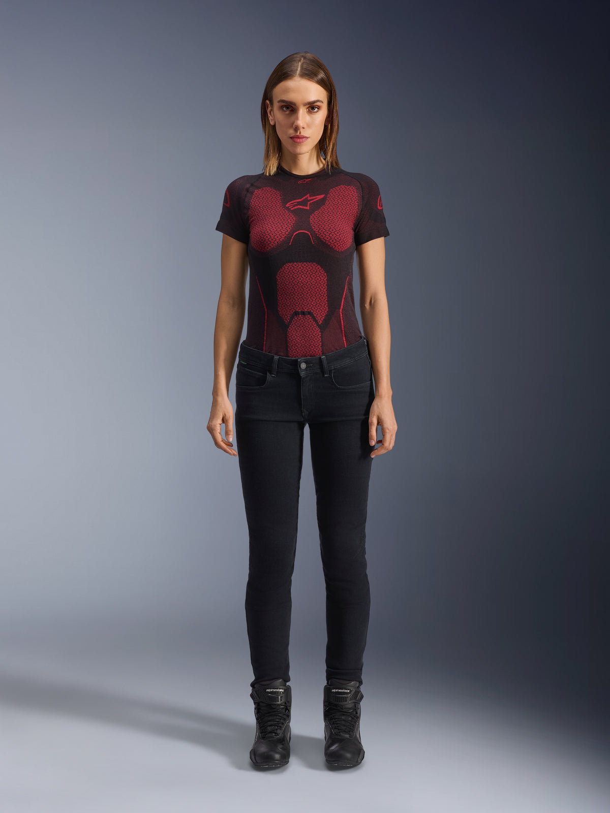 Alpinestars Daisy V3 dames motorjeans, Rinse Black, slim-fit motorbroek, gedragen door een model met een rood en zwart technisch T-shirt en zwarte motorlaarzen, casual urban motoruitrusting met een vrouwelijk silhouet en high-waisted ontwerp
