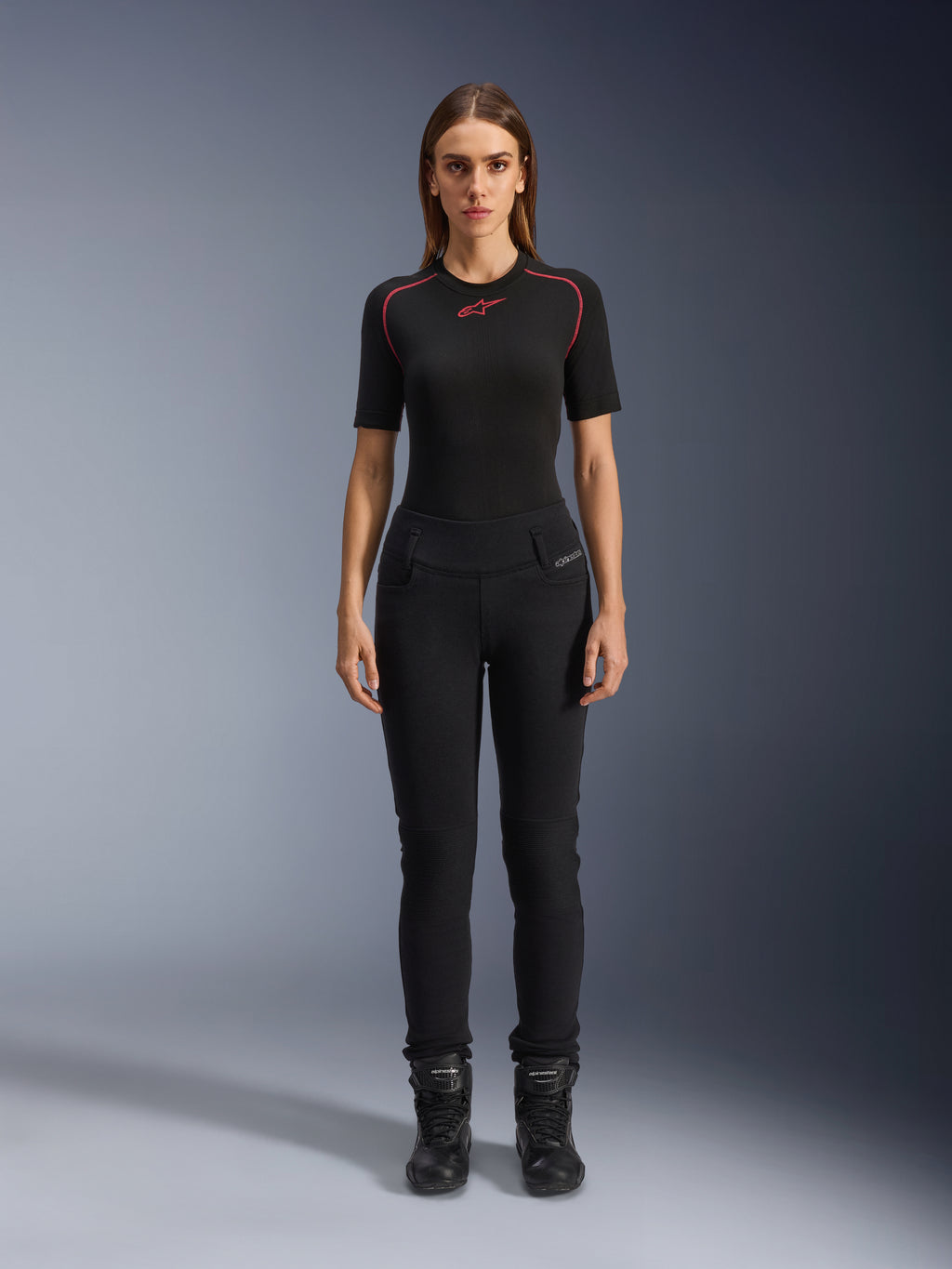 Alpinestars Banshee dameslegging, zwarte motorlegging, nauwsluitende anatomische pasvorm, gedragen door een vrouwelijk model met een zwarte basislaag en motorlaarzen, voorzien van geribbelde kniepanelen en een hoge taille voor urban rijden.