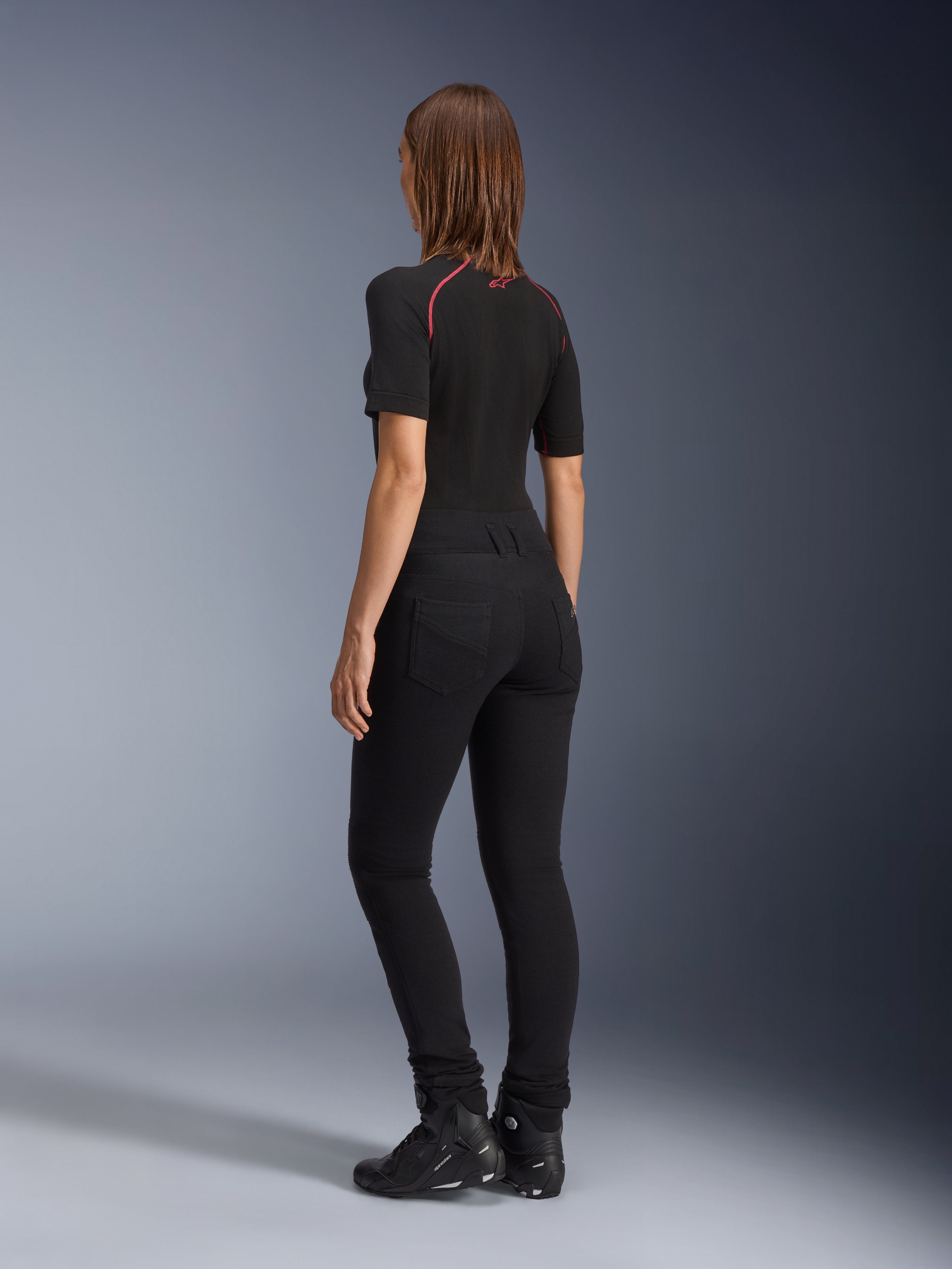 Alpinestars Banshee dames leggings, zwart, achteraanzicht met nauwsluitende anatomische stretchpasvorm en achterzakken, gedragen met een zwart shirt met korte mouwen en motorlaarzen, stijlvolle urban motorkleding voor dames