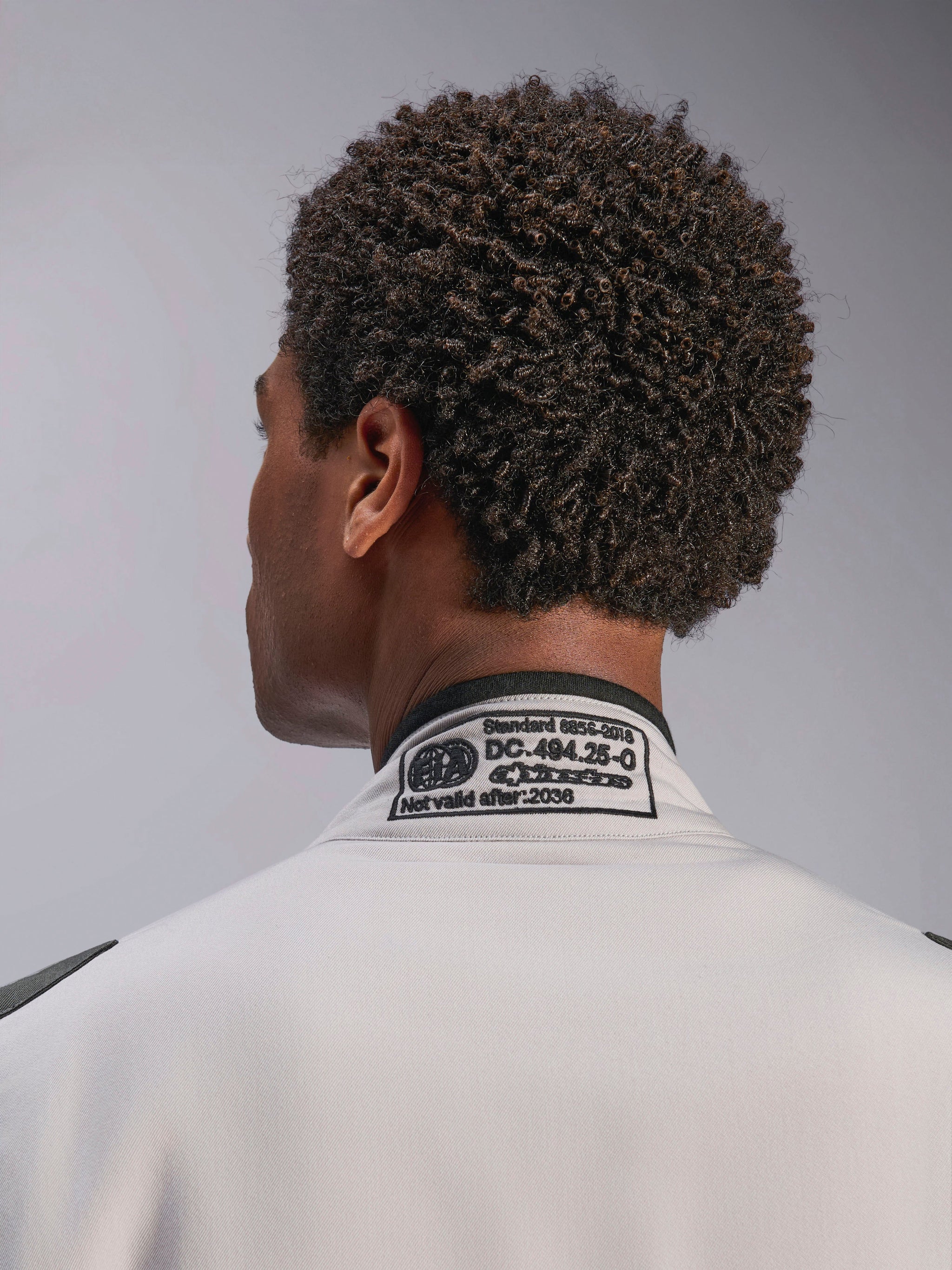 Alpinestars GP Race V3-pak FIA, Silver Anthracite, close-up van de achterkant van de kraag met het geborduurde FIA 8856-2018 certificeringslabel, toont de naleving van de veiligheidsnormen voor autorace-uitrusting