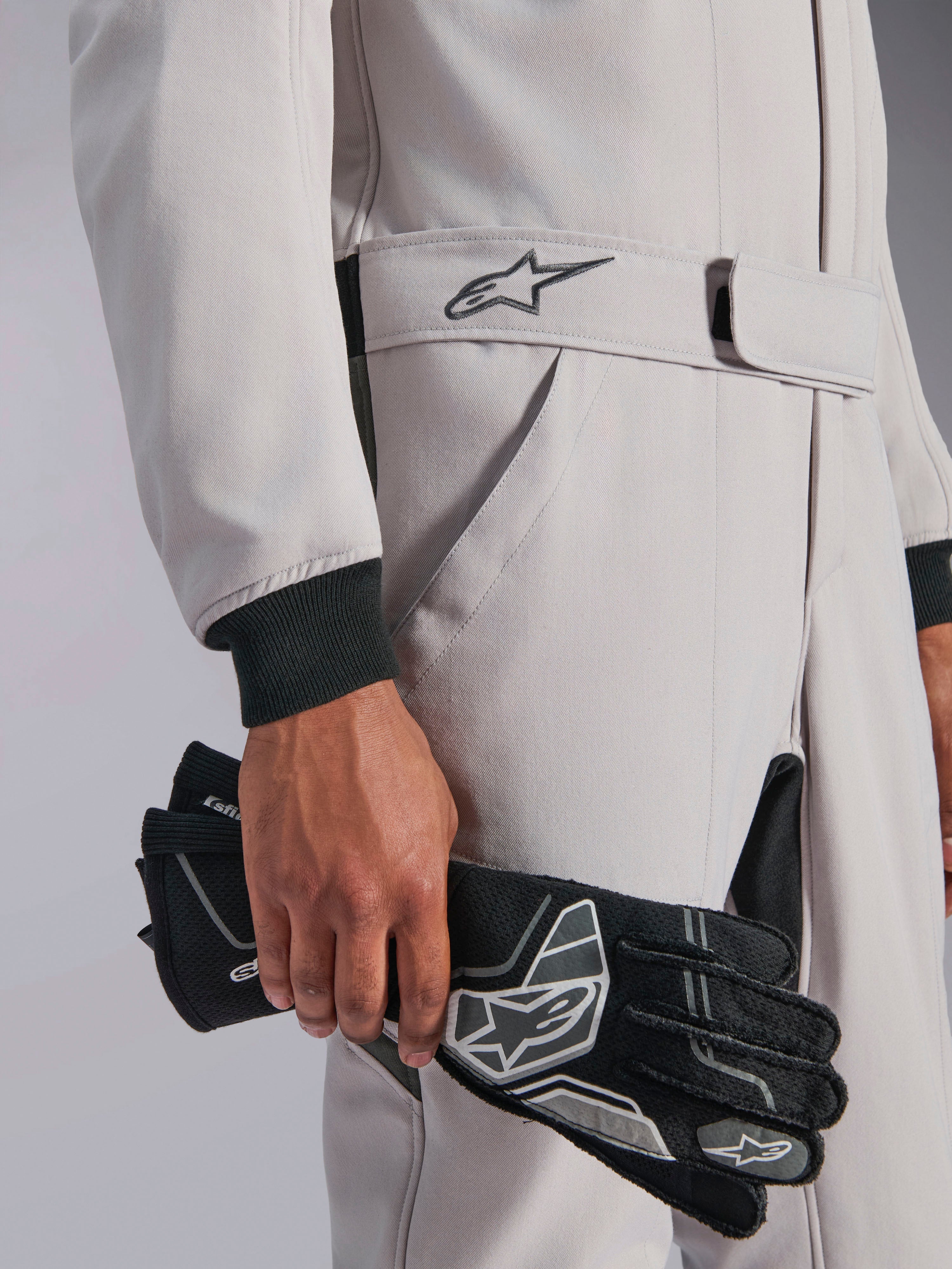 Alpinestars GP Race V3 Suit FIA, Auto Racing Suit, Silver Anthracite, held with black racing gloves, featuring adjustable belted waist with embroidered star logo, black ribbed cuffs, clean and professional motorsport design