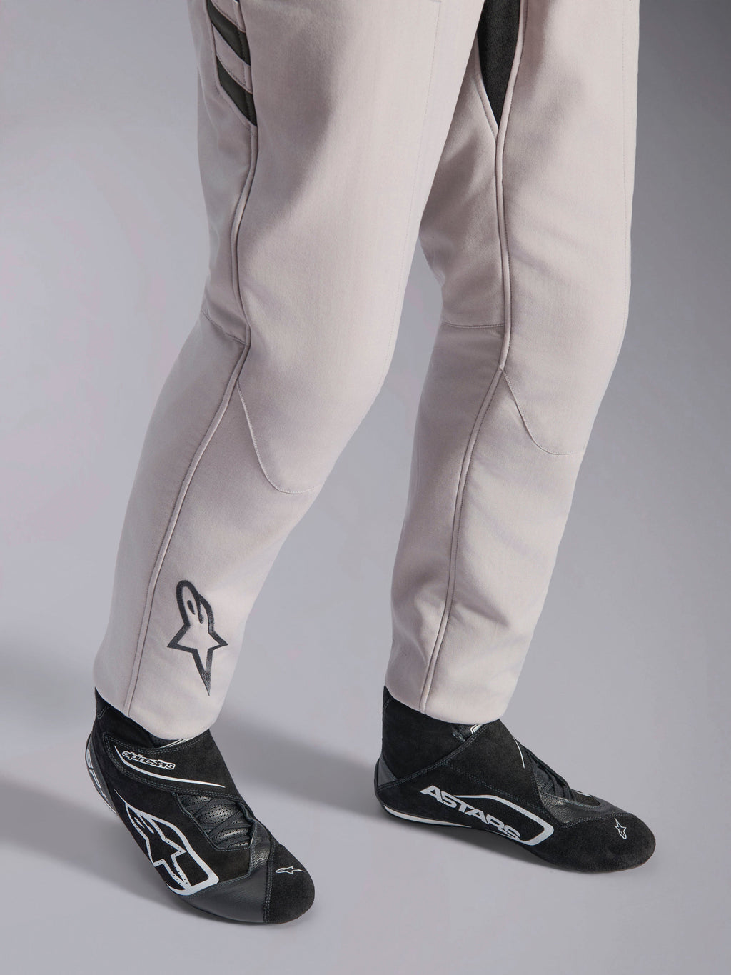 Alpinestars GP Race V3 Suit FIA, Silver Anthracite auto racing suit, detail shot of lower legs and black racing boots, featuring the black Astars logo on the calf, professional motorsport gear with ribbed cuffs