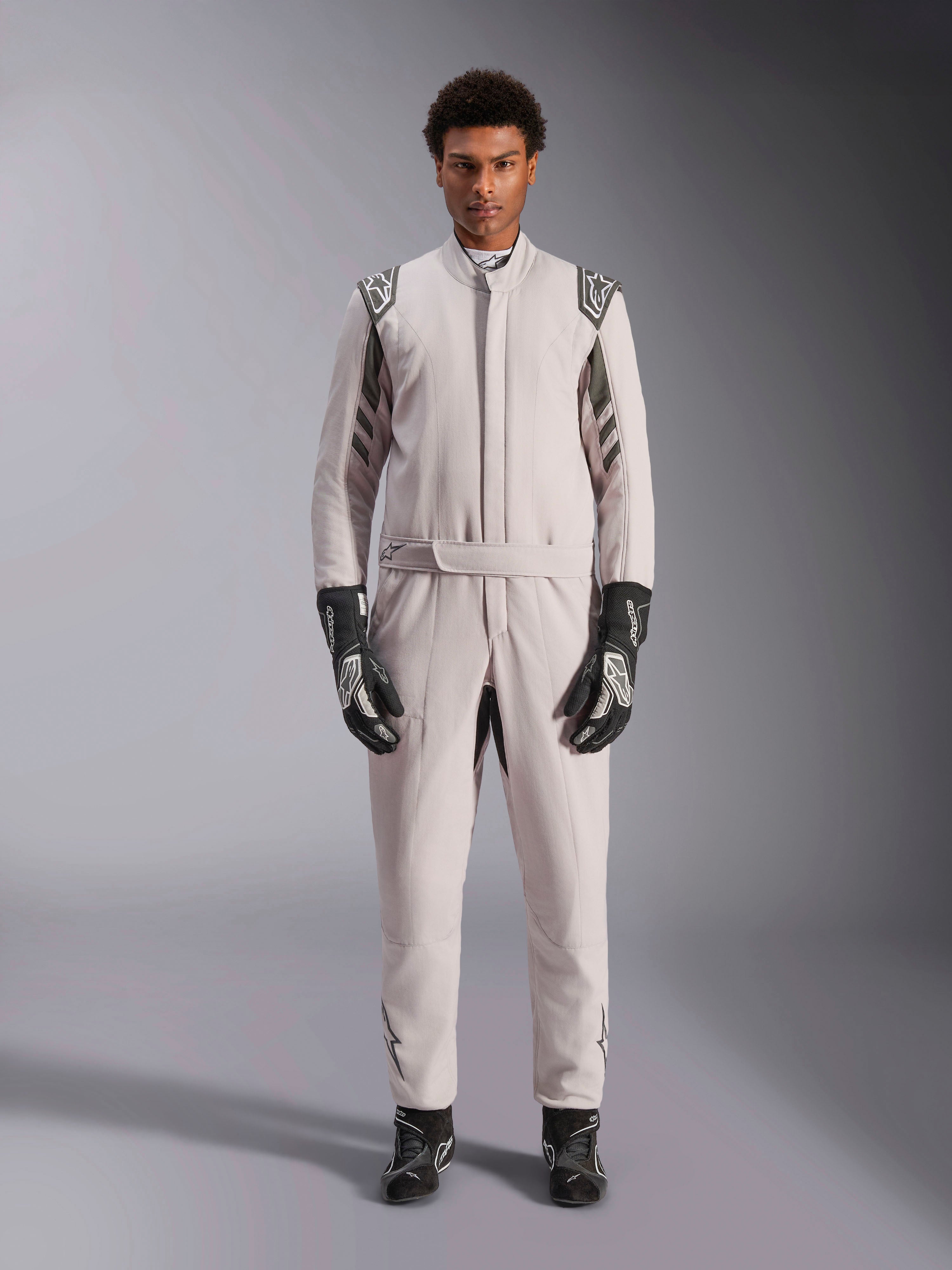 Alpinestars GP Race V3 Pak FIA in Silver Anthracite, eendelig autoracepak gedragen door een model, voorzien van donkergrijze epauletten en accenten, gecombineerd met zwarte racehandschoenen en -laarzen, professionele beschermende kleding voor de motorsport.
