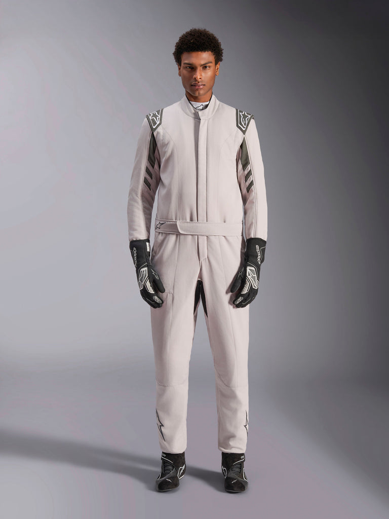 Alpinestars GP Race V3 Pak FIA in Silver Anthracite, eendelig autoracepak gedragen door een model, voorzien van donkergrijze epauletten en accenten, gecombineerd met zwarte racehandschoenen en -laarzen, professionele beschermende kleding voor de motorsport.