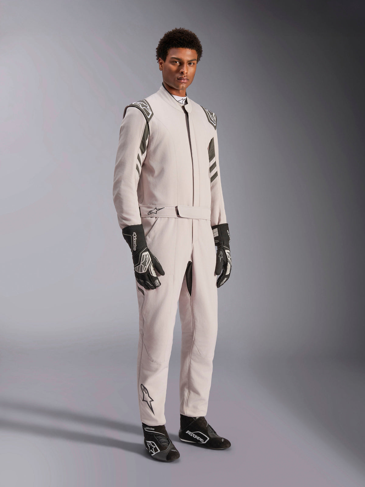 Alpinestars GP Race V3 Pak FIA, zilver antraciet racepak, eendelig coureurspak met schouder-epauletten en een taille met riem, gedragen met bijpassende zwart-witte racehandschoenen en laarzen, strak ontwerp voor professionele autosport