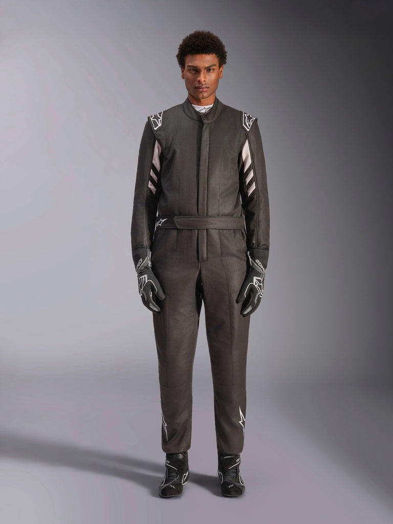 Alpinestars GP Race V3 Pak FIA, autoracepak, zwart en zilver, vooraanzicht van een coureur in volledige race-uitrusting inclusief handschoenen en laarzen, professioneel motorsportontwerp met Alpinestars-branding op de schouders en riem