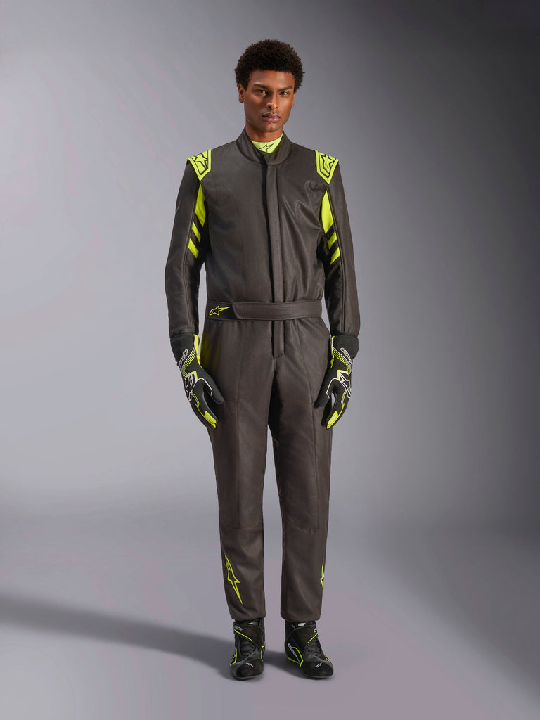 Alpinestars GP Race V3 Pak FIA, autoracepak, zwart en fluogeel, gedragen door een model met bijpassende racehandschoenen en laarzen, voorzien van felgele accenten op de schouders, taille en mouwen, professionele motorsportuitrusting