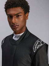 Alpinestars Hypertech V3 Pak, Black Dark Shadow autoracepak, close-up van mannelijk model, zilveren schouderlogo's, hoge kraag met wit Alpinestars mock-neck shirt, professionele motorsport beschermende kleding