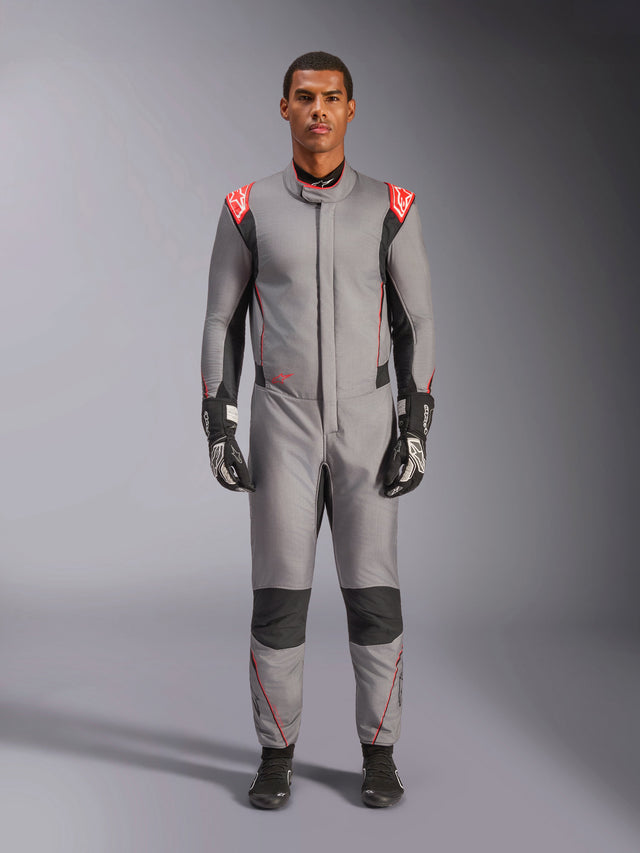 Alpinestars Hypertech V3 Suit, professional auto racing suit in Mid Gray Black and Red Fluo, worn by a model with black racing gloves and shoes, featuring an athletic-slim fit, red fluo shoulder accents, and black panels on the knees and sides.