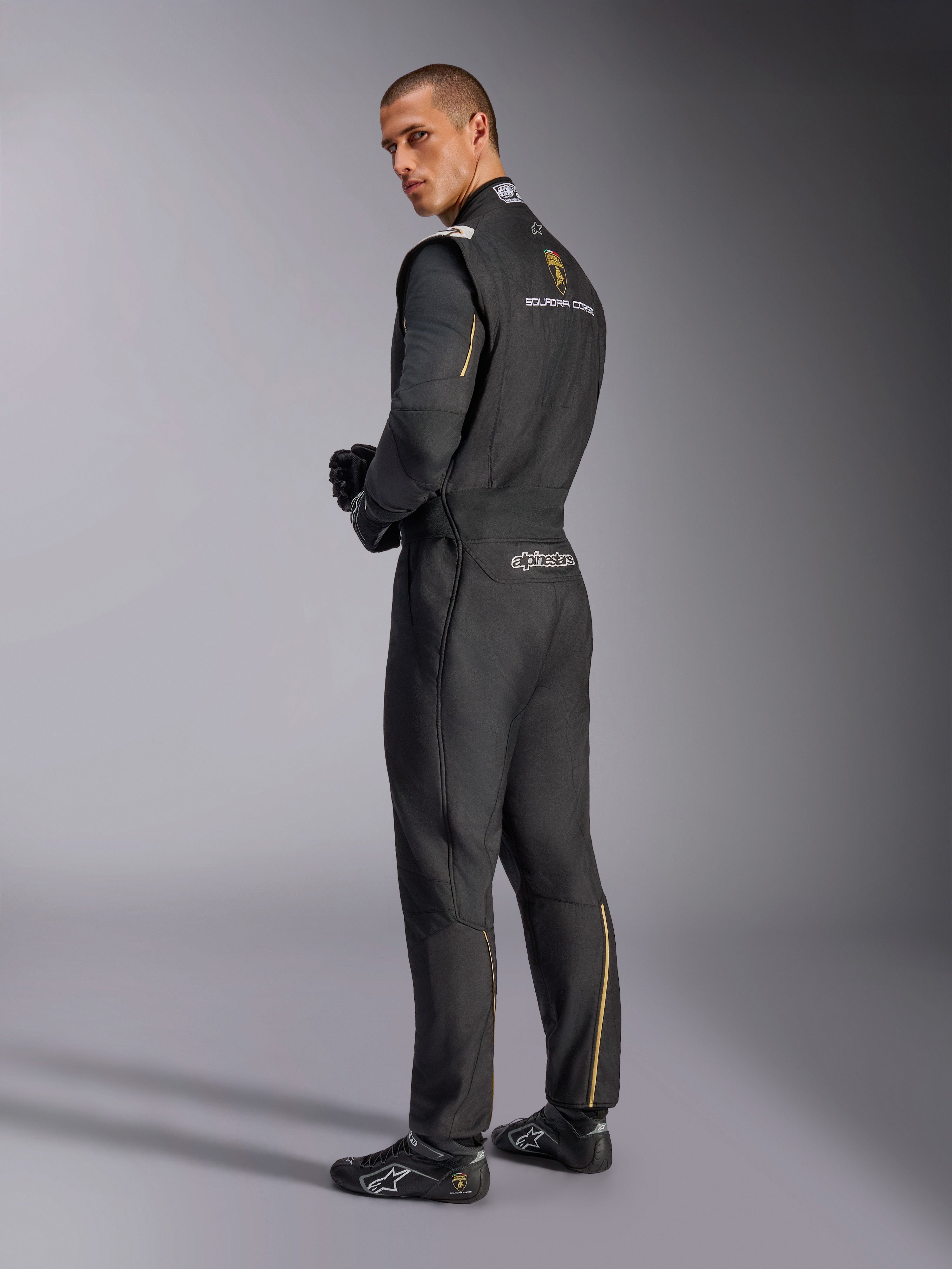 Alpinestars Limited Edition Lamborghini GP Tech V4 Suit, Professional Auto Racing Suit, Black with Silver and Gold accents, back view showing Lamborghini Squadra Corse and Alpinestars branding, worn with black racing gloves and footwear, sleek motorsport design