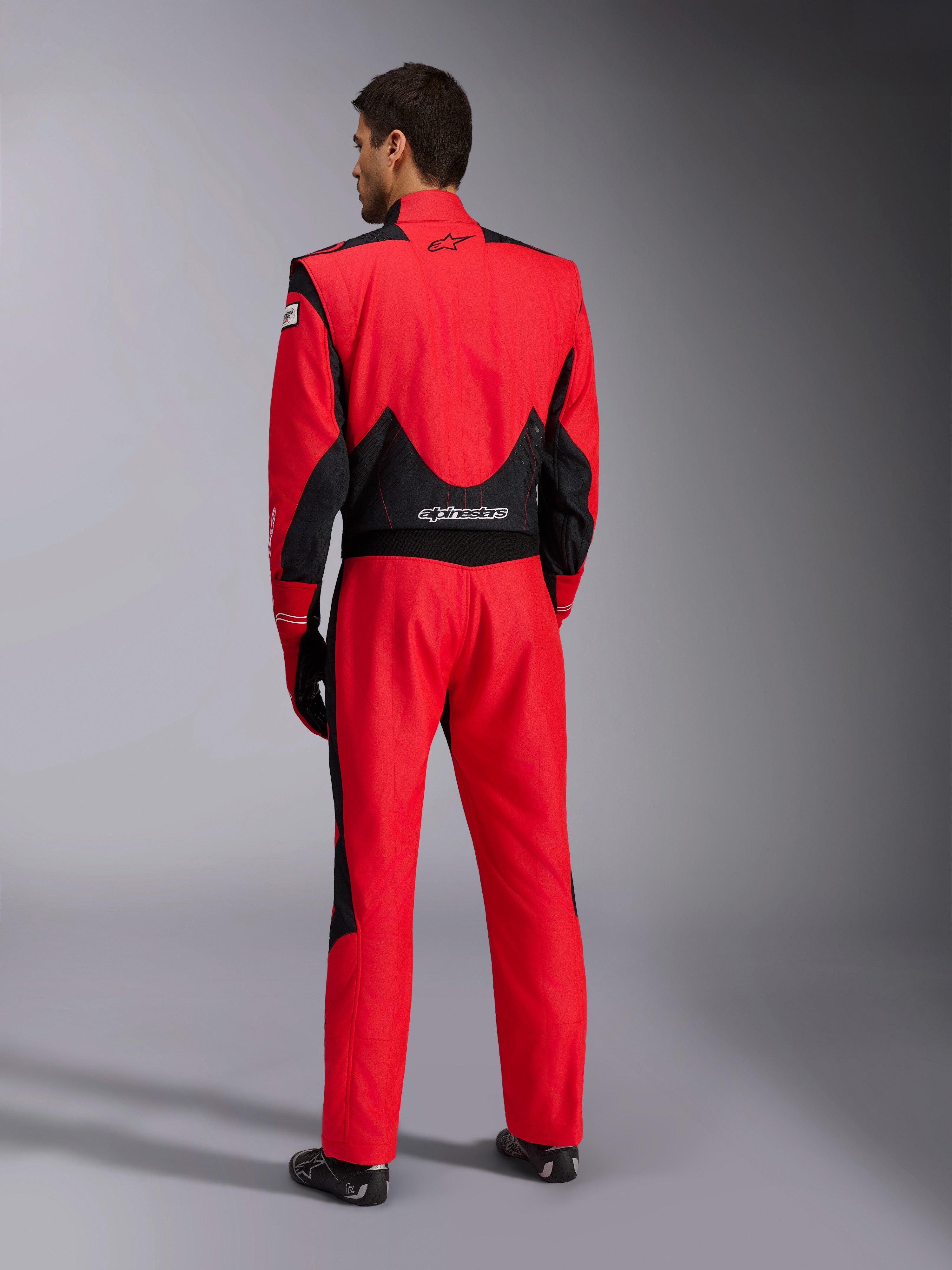 Volledig achteraanzicht van het Alpinestars GP Pro Comp V2 FIA racepak, rood en zwart, voorzien van ademende zwarte mesh-panelen op de schouders en onderrug, wit Alpinestars-logo, gedragen met bijpassende racehandschoenen en laarzen, professionele motorsportuitrusting