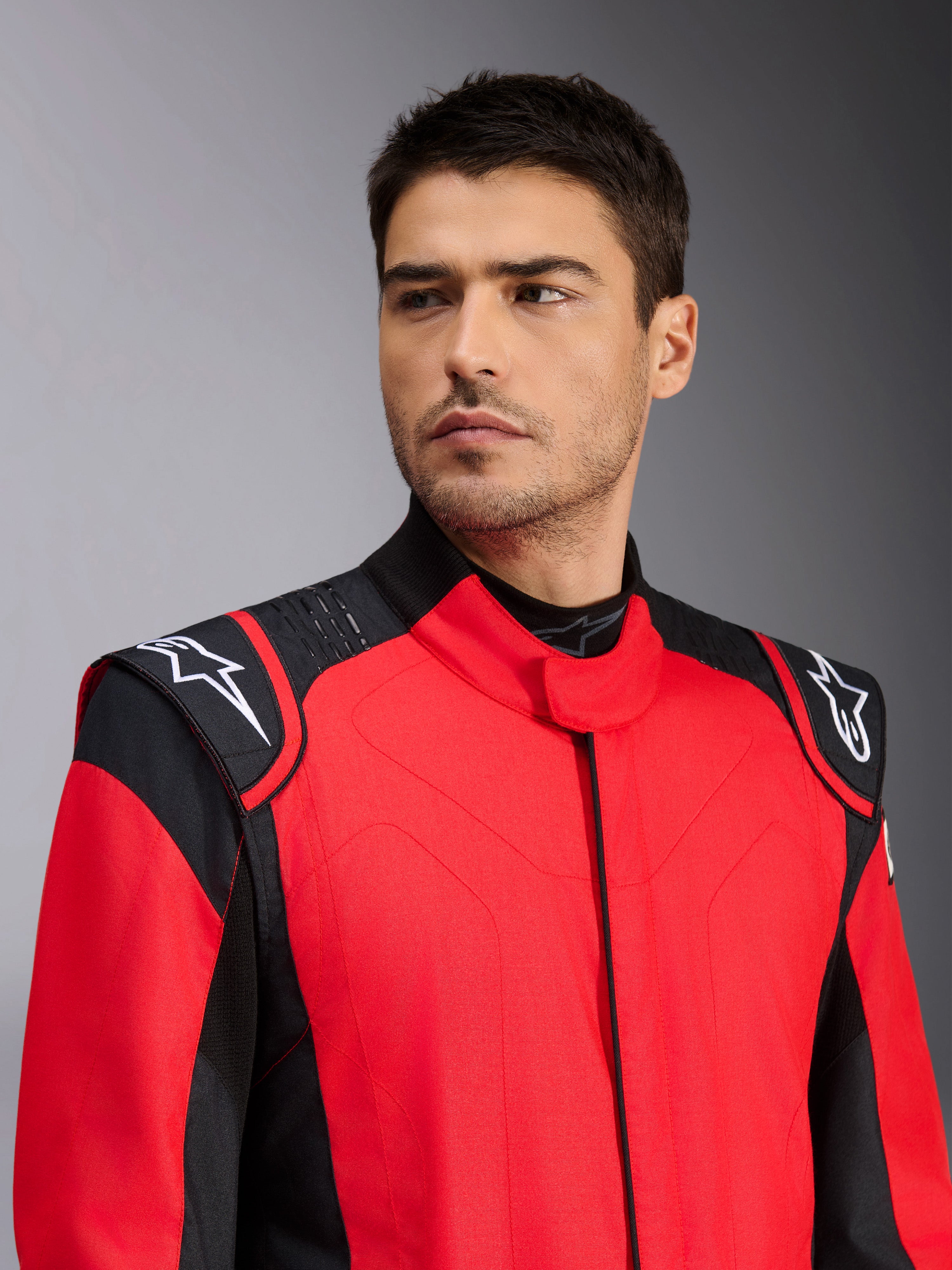 Alpinestars GP Pro Comp V2 FIA autoracepak, rood en zwart, voorzien van witte Astars-logo's op de schouders en siliconen griptechnologie-details, professionele motorsportkleding, mannelijk model draagt de outfit