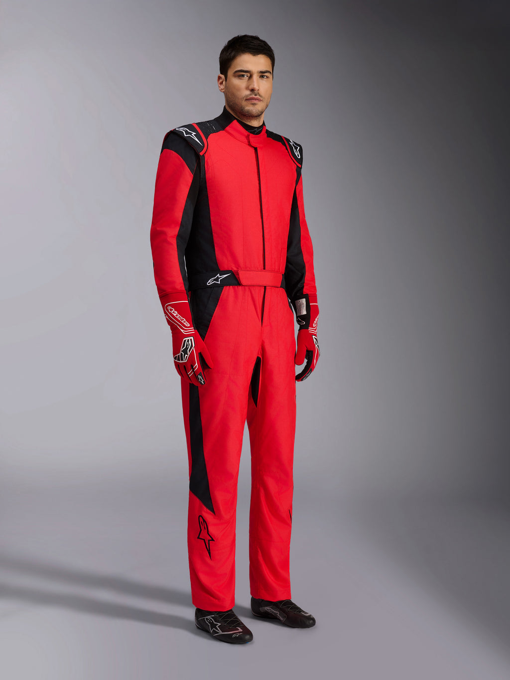 Alpinestars GP Pro Comp V2 FIA racepak, rood en zwart professioneel autoracepak, gedragen met bijpassende rood-witte handschoenen en zwarte raceschoenen, studioportret van volledige beschermende motorsportuitrusting