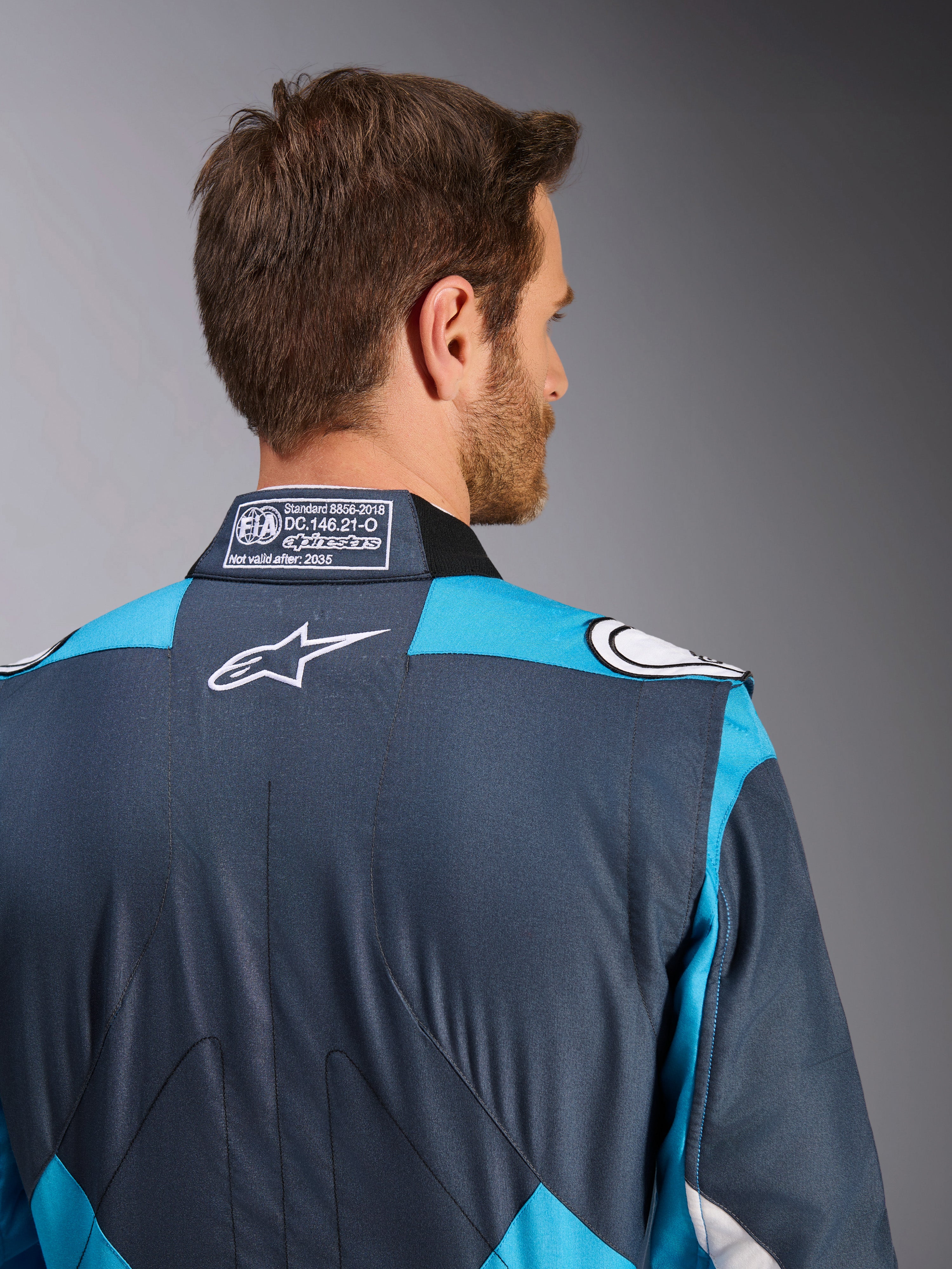 Alpinestars GP Pro Comp V2 Pak - FIA, heren-autoracepak, asfalt en cyaan, wit logo en FIA-homologatielabel op de kraag.
