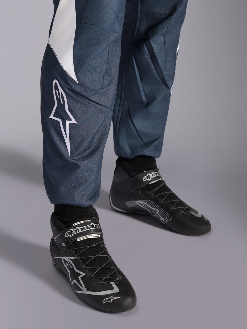 Alpinestars GP Pro Comp V2 FIA-pak, asphalt en cyan, close-up van wit sterlogo en zwarte raceschoenen