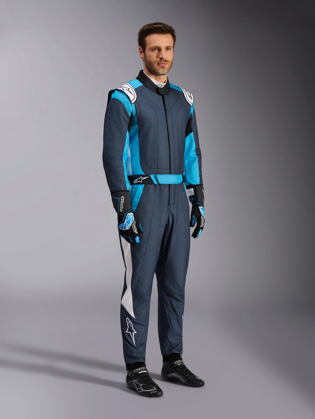 Alpinestars GP Pro Comp V2 FIA pak, professionele autorace-uitrusting in asphalt en cyaan, gedragen door een man.