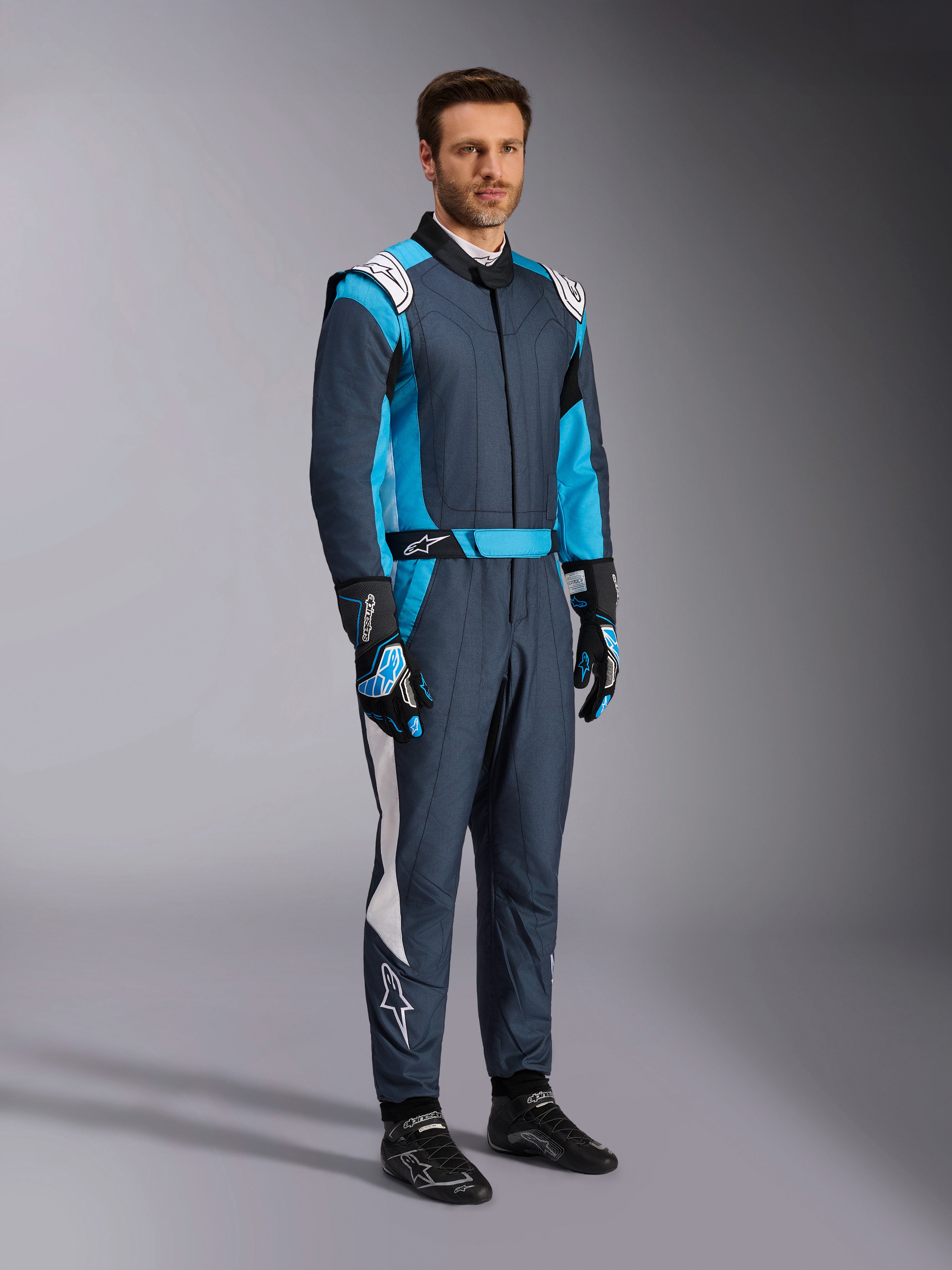 Alpinestars GP Pro Comp V2 FIA pak, professionele autorace-uitrusting in asphalt en cyaan, gedragen door een man.