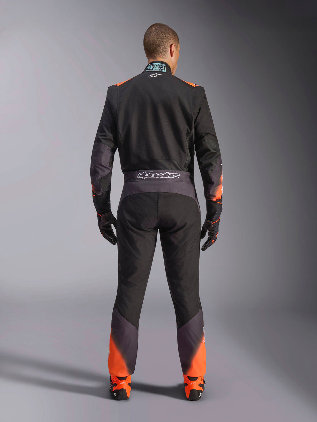 Alpinestars KMX-5 V3 pak, zwart en oranje fluo eendelig kartpak voor heren, FIA-gecertificeerd, achteraanzicht met branding.