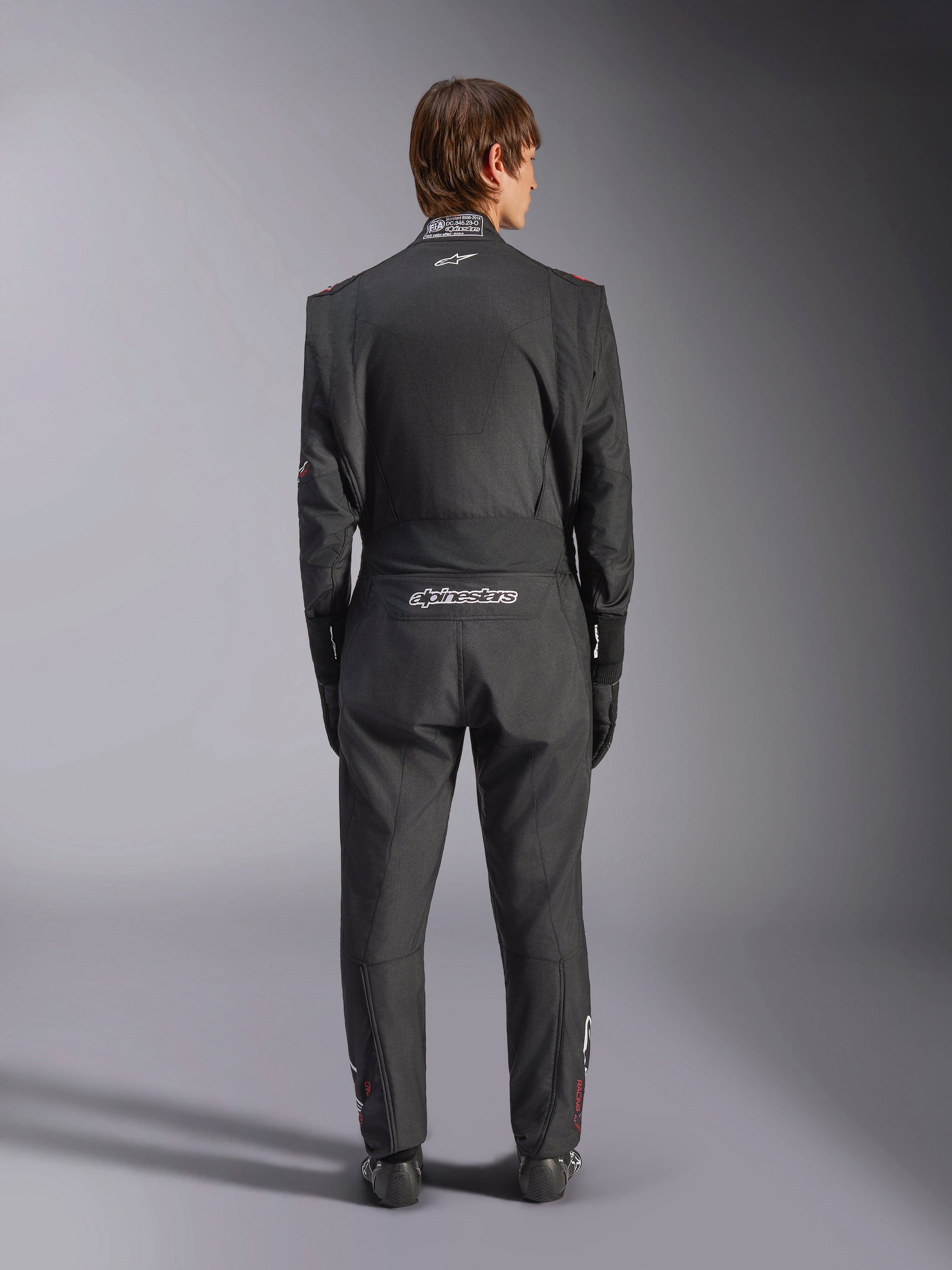 Alpinestars GP Tech V4-pak, autoracepak, zwart en wit, achteraanzicht met witte Alpinestars-branding en FIA-certificering op de kraag, gestroomlijnde ergonomische pasvorm voor professionele bescherming van de coureur