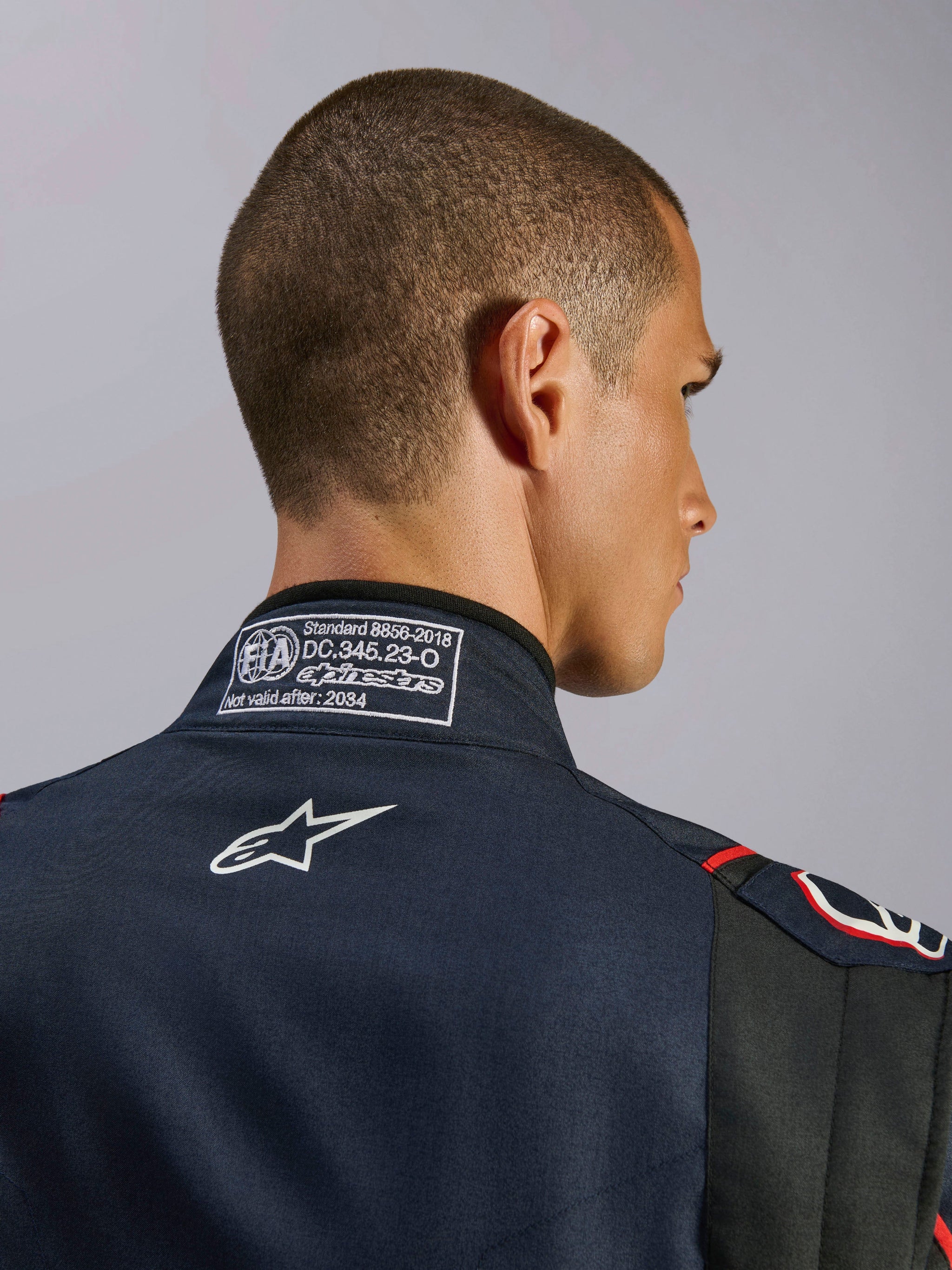Alpinestars GP Tech V4 Suit in Blue Navy Black Red, close-up van de achterkraag met het FIA 8856-2018-certificeringslabel en wit geborduurd Alpinestars-logo, detail van een hoogwaardig autoracepak