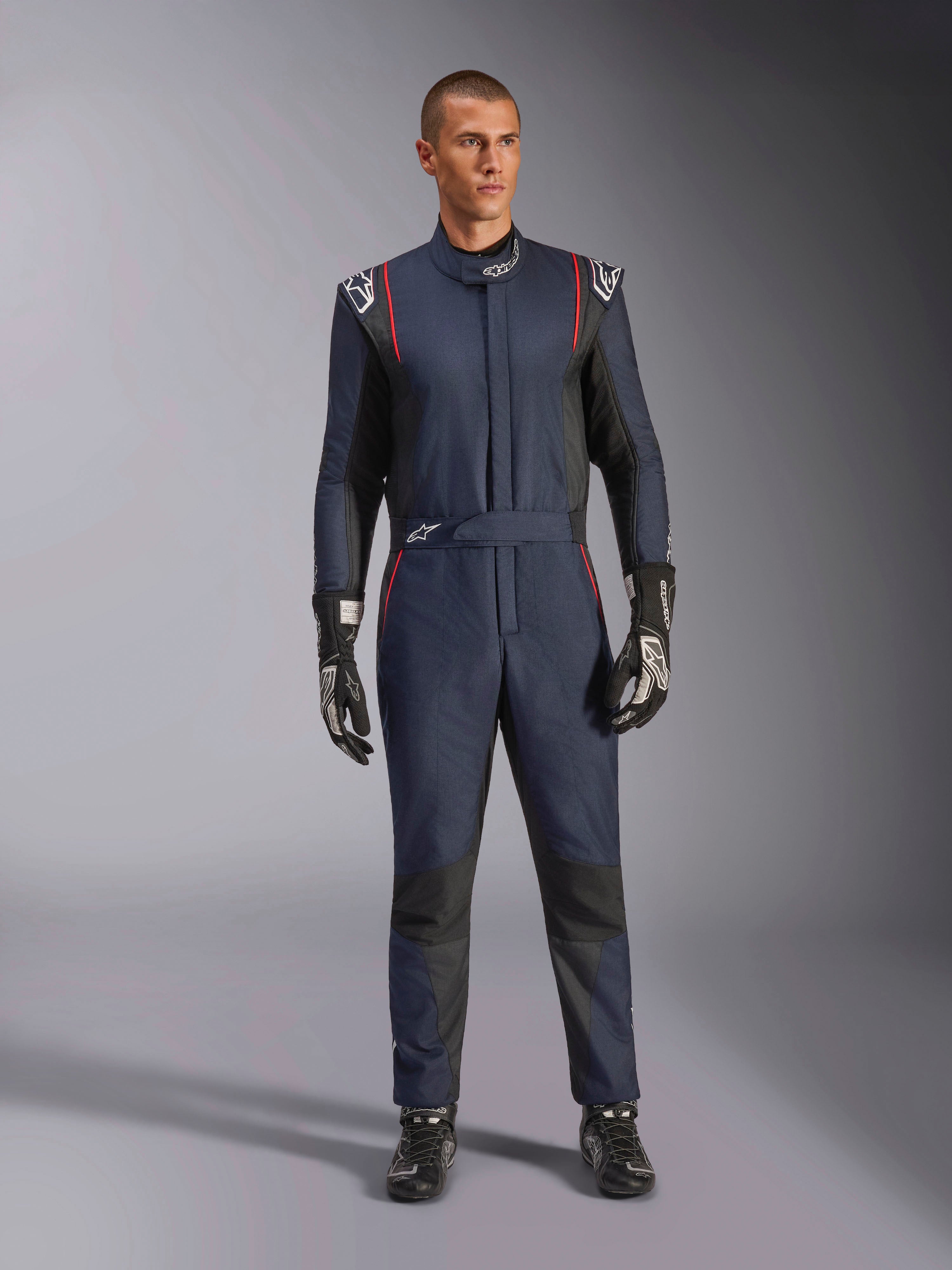 Alpinestars GP Tech V4 Suit, professioneel autoracepak in donkerblauw en zwart met rode biezen, eendelig FIA-gecertificeerd racepak, gedragen met zwarte racehandschoenen en raceschoenen, motorsport kleding voor coureurs