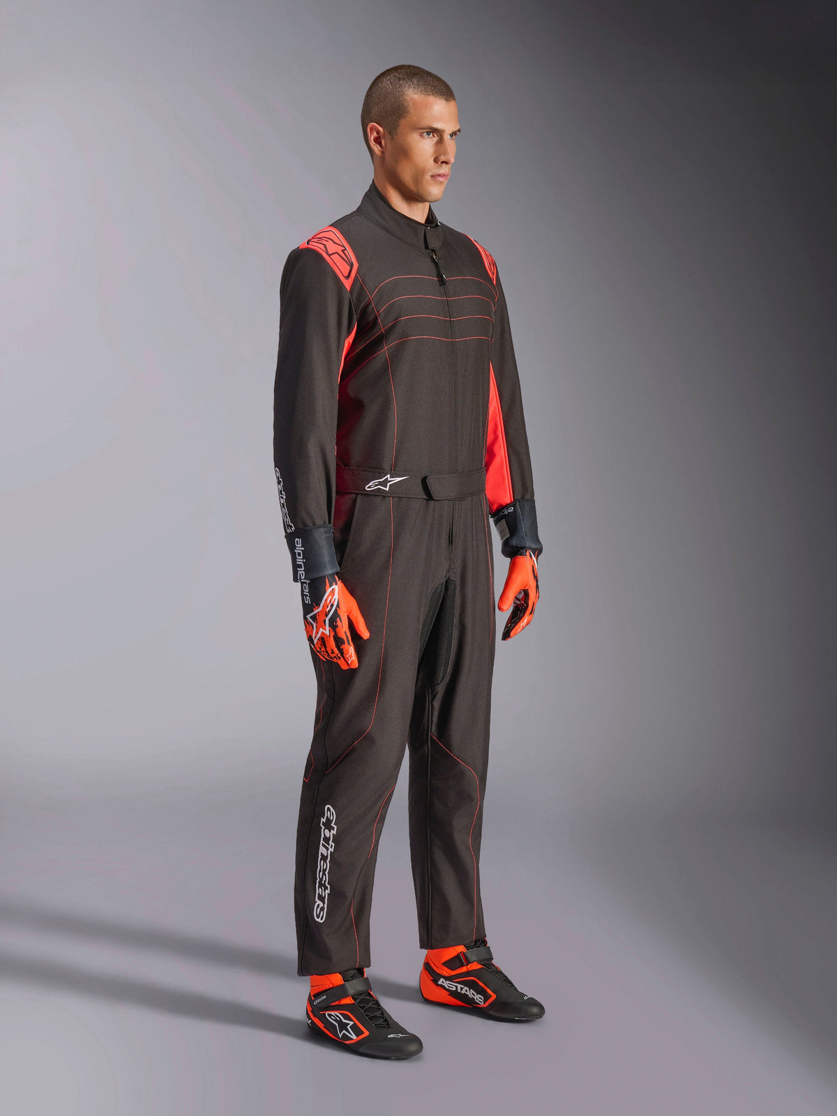Alpinestars KMX-9 V3 Pak, kartpak, zwart rood fluo, gedragen door een model met oranje handschoenen en zwarte raceschoenen, voorzien van rode stiksels, schouderaccenten en witte logo's, atletisch ontwerp voor professioneel racen