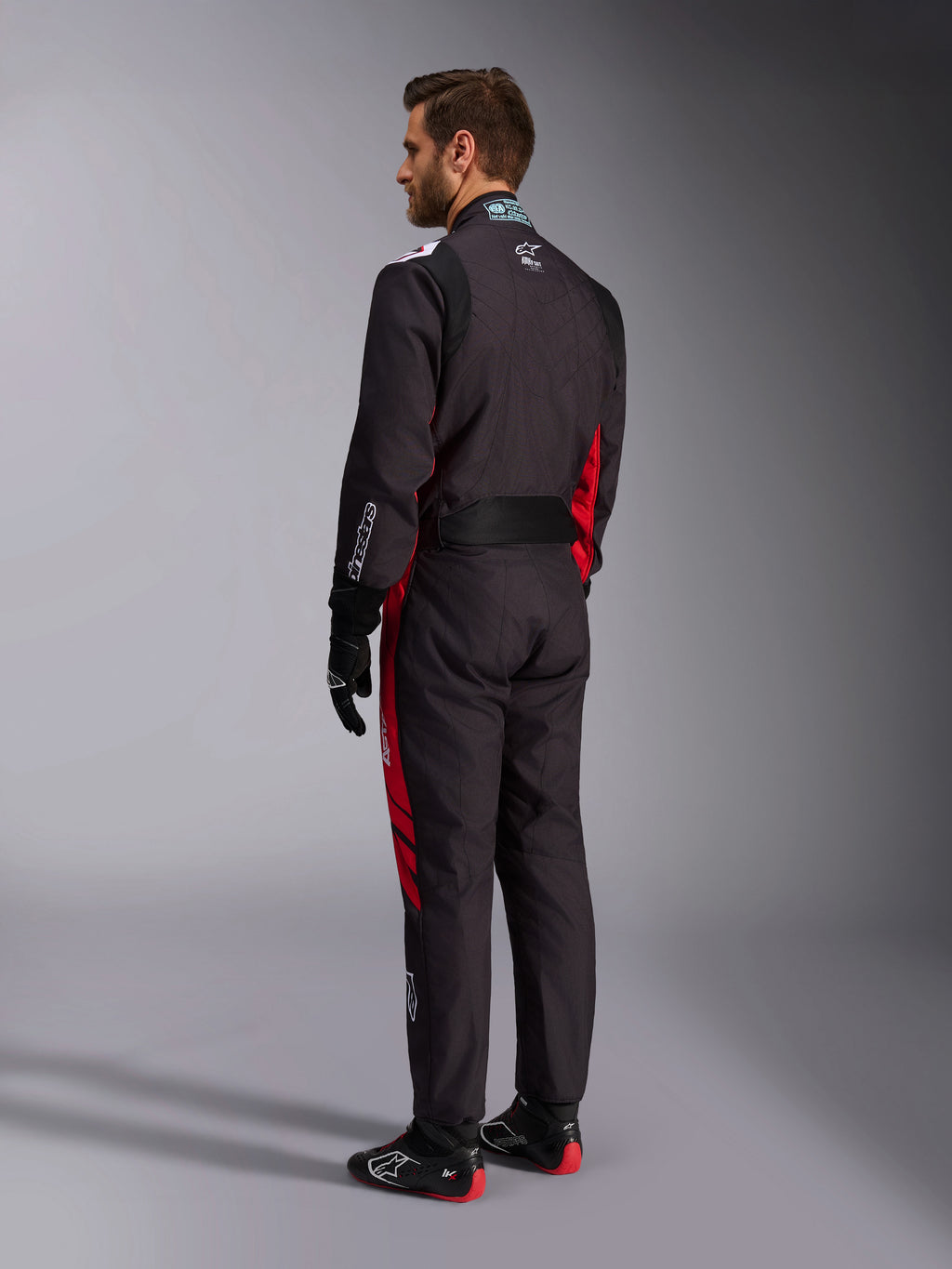 Alpinestars KMX-9 V3 Graphic 3 Suit, zwart en rood, achteraanzicht van model in volledige kartuitrusting inclusief zwarte handschoenen en raceschoenen, met rode zijpanelen en witte logodetails