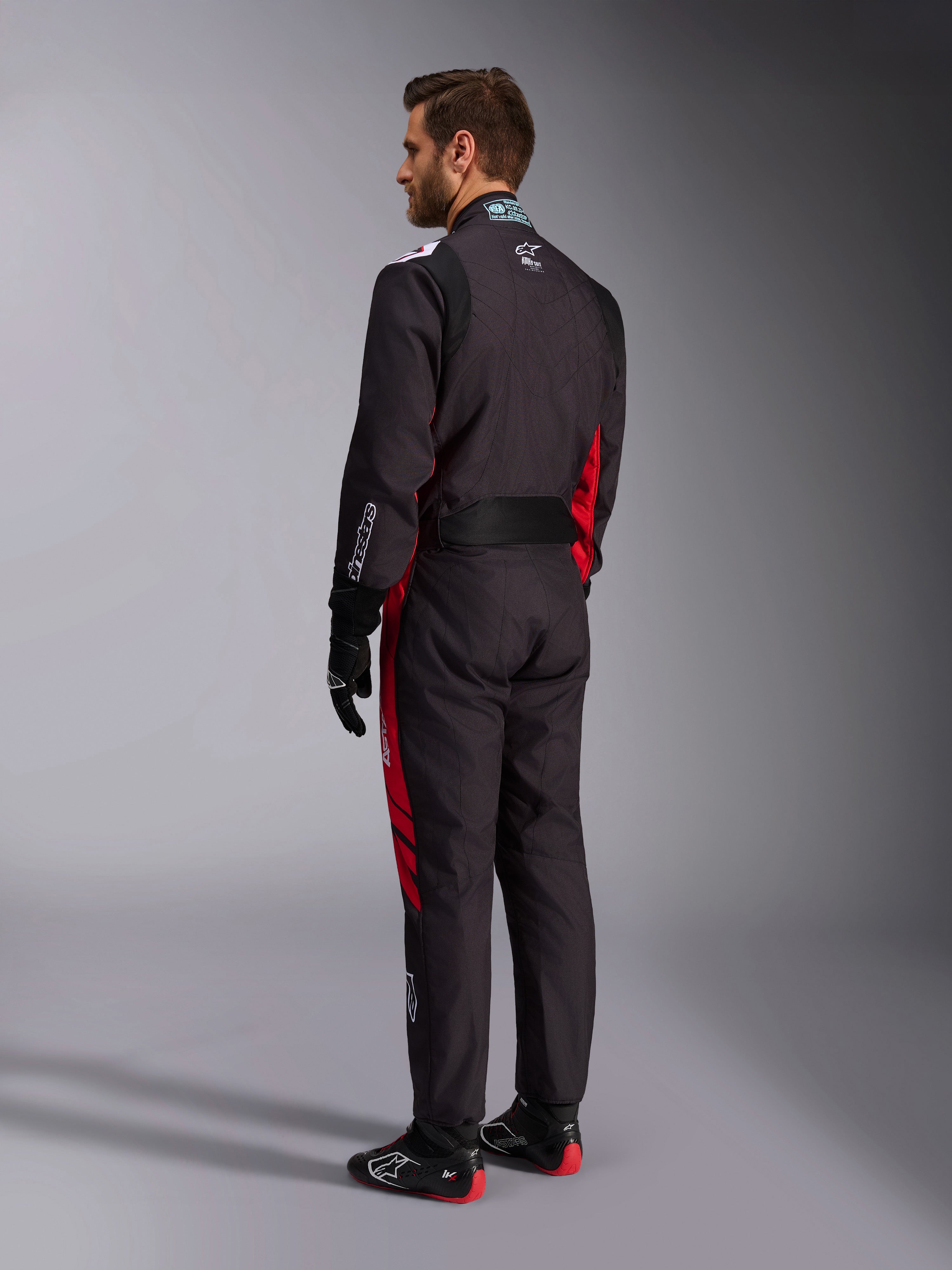 Alpinestars KMX-9 V3 Graphic 3 Suit, zwart en rood, achteraanzicht van model in volledige kartuitrusting inclusief zwarte handschoenen en raceschoenen, met rode zijpanelen en witte logodetails