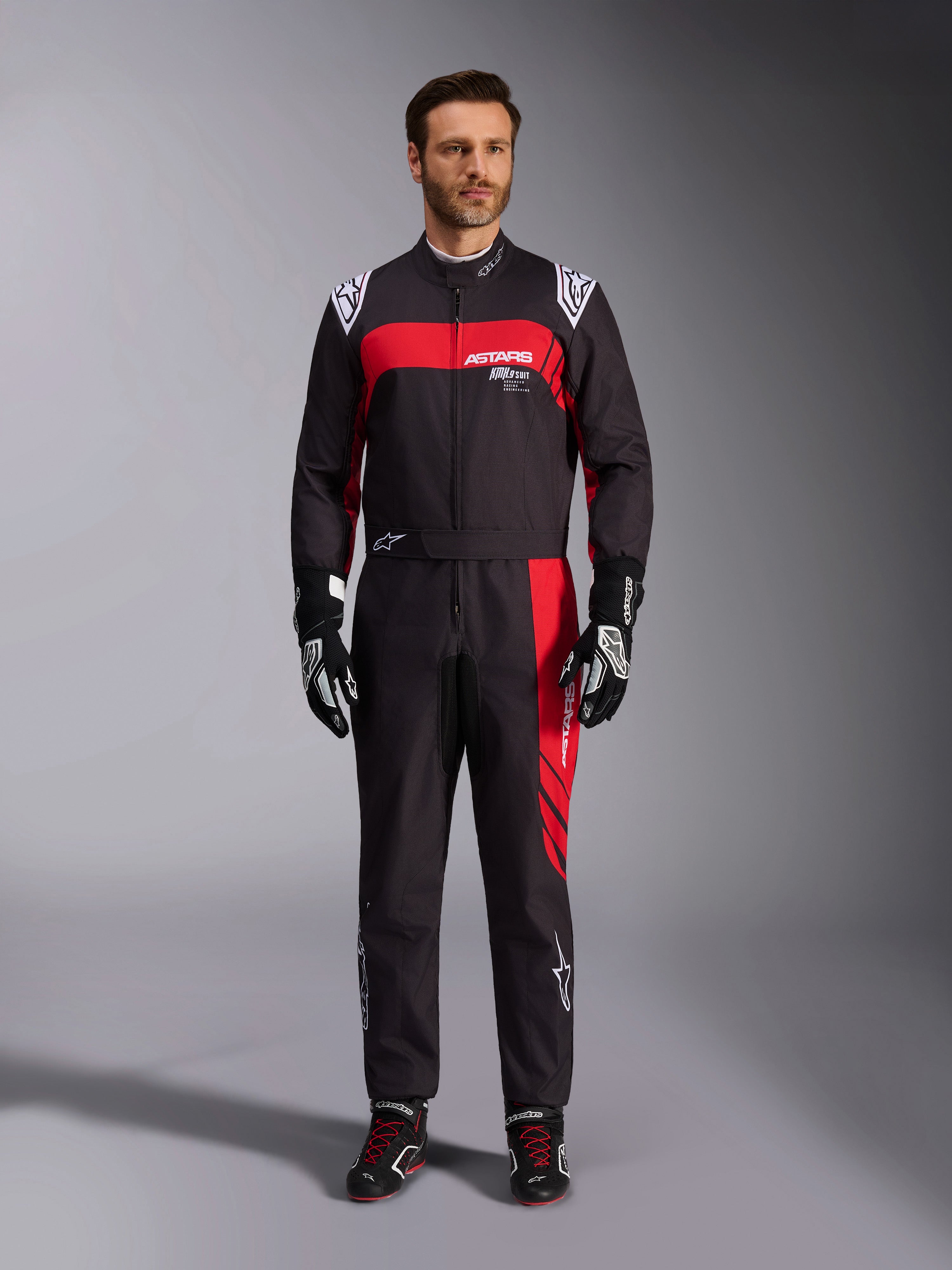 Alpinestars KMX-9 V3 Graphic 3 pak, kartingpak, zwart en rood, volledig vooraanzicht gedragen door een model, met opvallende rode grafische panelen en witte logo's, gecombineerd met zwarte racehandschoenen en schoenen, professionele motorsportkleding