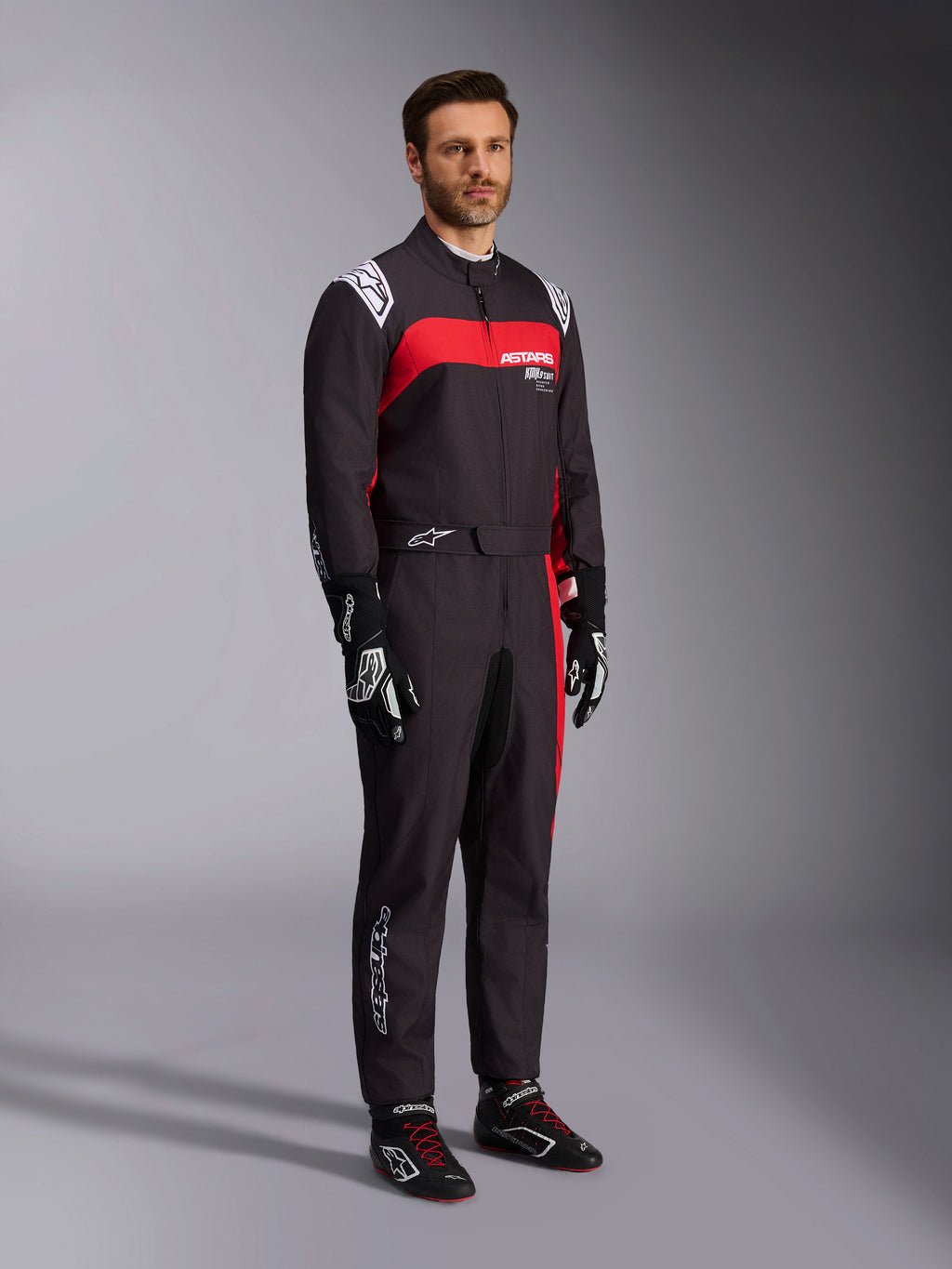 Alpinestars KMX-9 V3 Graphic 3 pak, kartpak, zwart en rood, voorzien van witte schouder-epauletten en rode branding op de borst, gecombineerd met zwarte racehandschoenen en schoenen met rode veters, professionele motorsportkleding, gedragen door een mannelijk model.