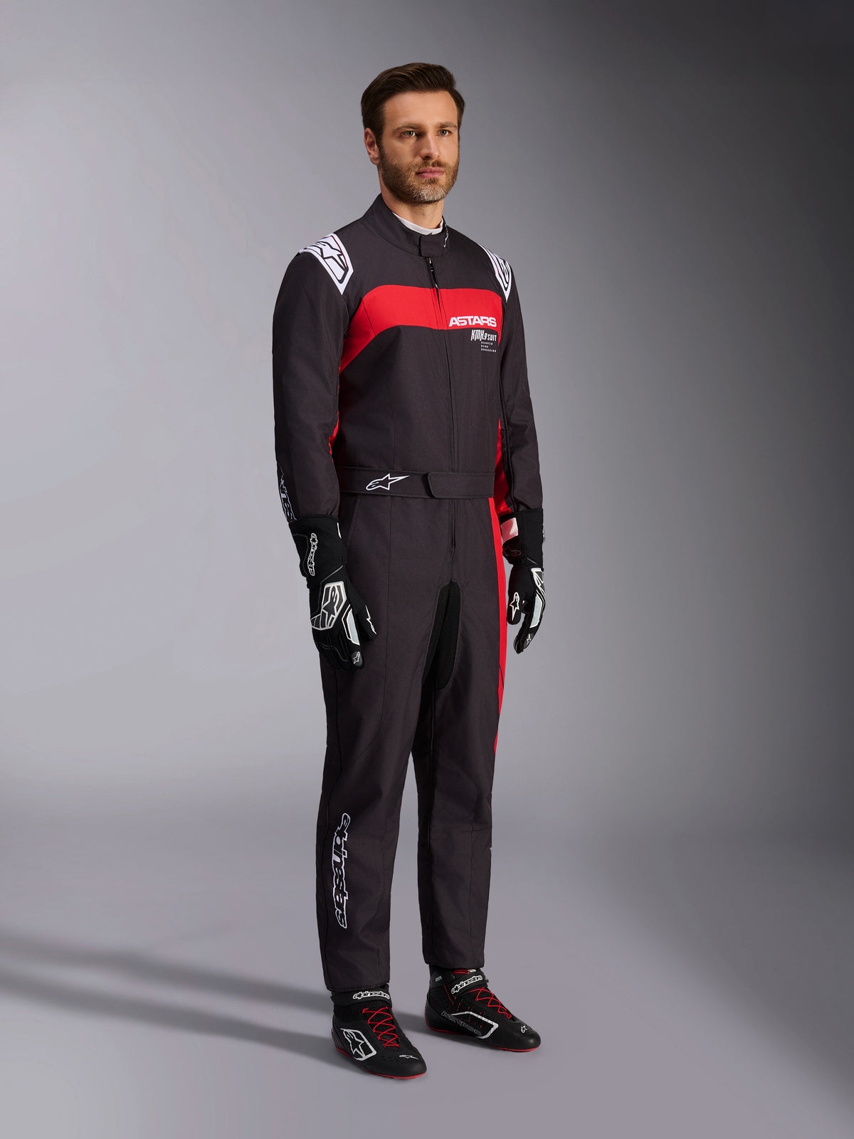 Alpinestars KMX-9 V3 Graphic 3 pak, kartpak, zwart en rood, voorzien van witte schouder-epauletten en rode branding op de borst, gecombineerd met zwarte racehandschoenen en schoenen met rode veters, professionele motorsportkleding, gedragen door een mannelijk model.