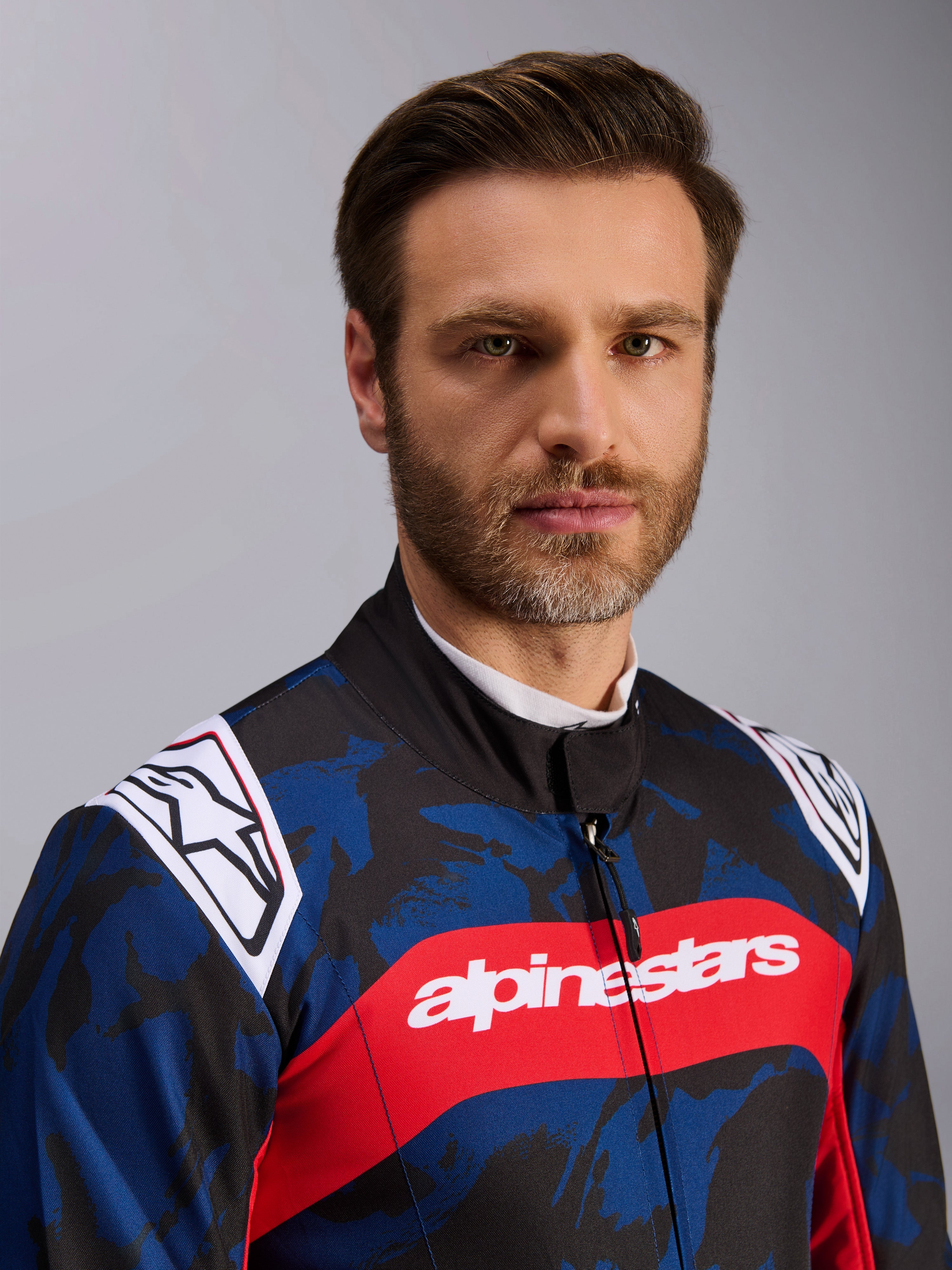 Alpinestars KMX-9 V3 Graphic 5 pak, kartpak in Navy Red, voorzien van een blauw en zwart camouflage grafisch patroon, een opvallende rode horizontale streep met witte Alpinestars tekst over de borst en witte logo's op de schouders, gedragen door een model in een studio-omgeving.