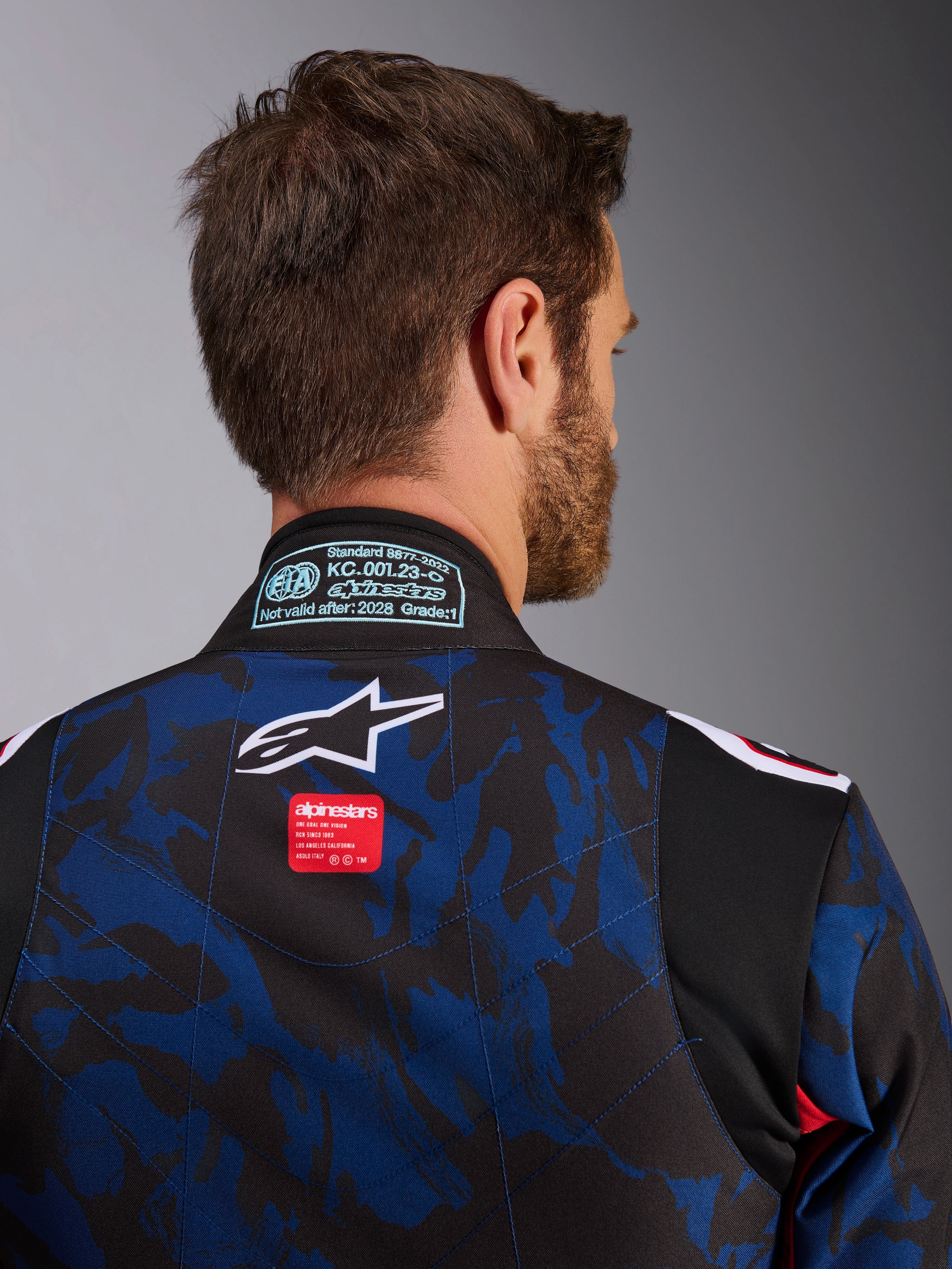 Close-up van Alpinestars KMX-9 V3 Graphic 5-pak, kartpak in Navy Red, voorzien van blauw en zwart camouflagepatroon, wit sterlogo en rood merklabel op de bovenrug, met FIA 8877-2022 certificeringspatch op de kraag