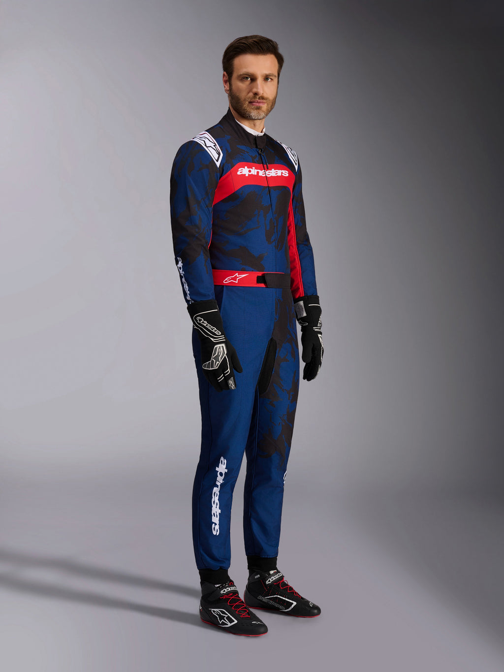 Alpinestars KMX-9 V3 Graphic 5 kartpak in Navy Red, marineblauw met donkere camouflage-graphics en een opvallend rood borstpaneel met witte branding, volledig lichaamsbeeld inclusief zwarte karthandschoenen en zwarte raceschoenen, professionele beschermende kartuitrusting