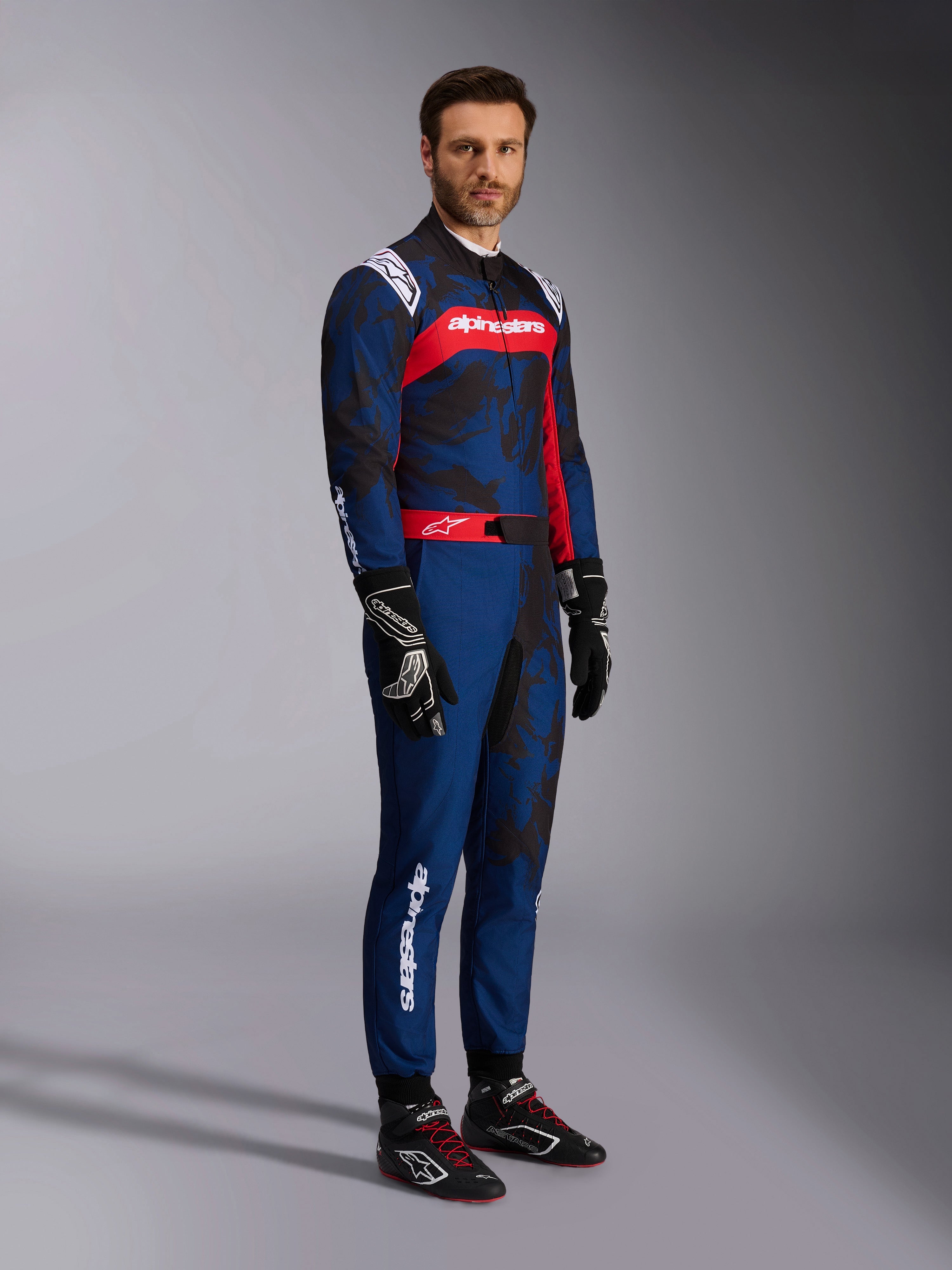 Alpinestars KMX-9 V3 Graphic 5 kartpak in Navy Red, marineblauw met donkere camouflage-graphics en een opvallend rood borstpaneel met witte branding, volledig lichaamsbeeld inclusief zwarte karthandschoenen en zwarte raceschoenen, professionele beschermende kartuitrusting