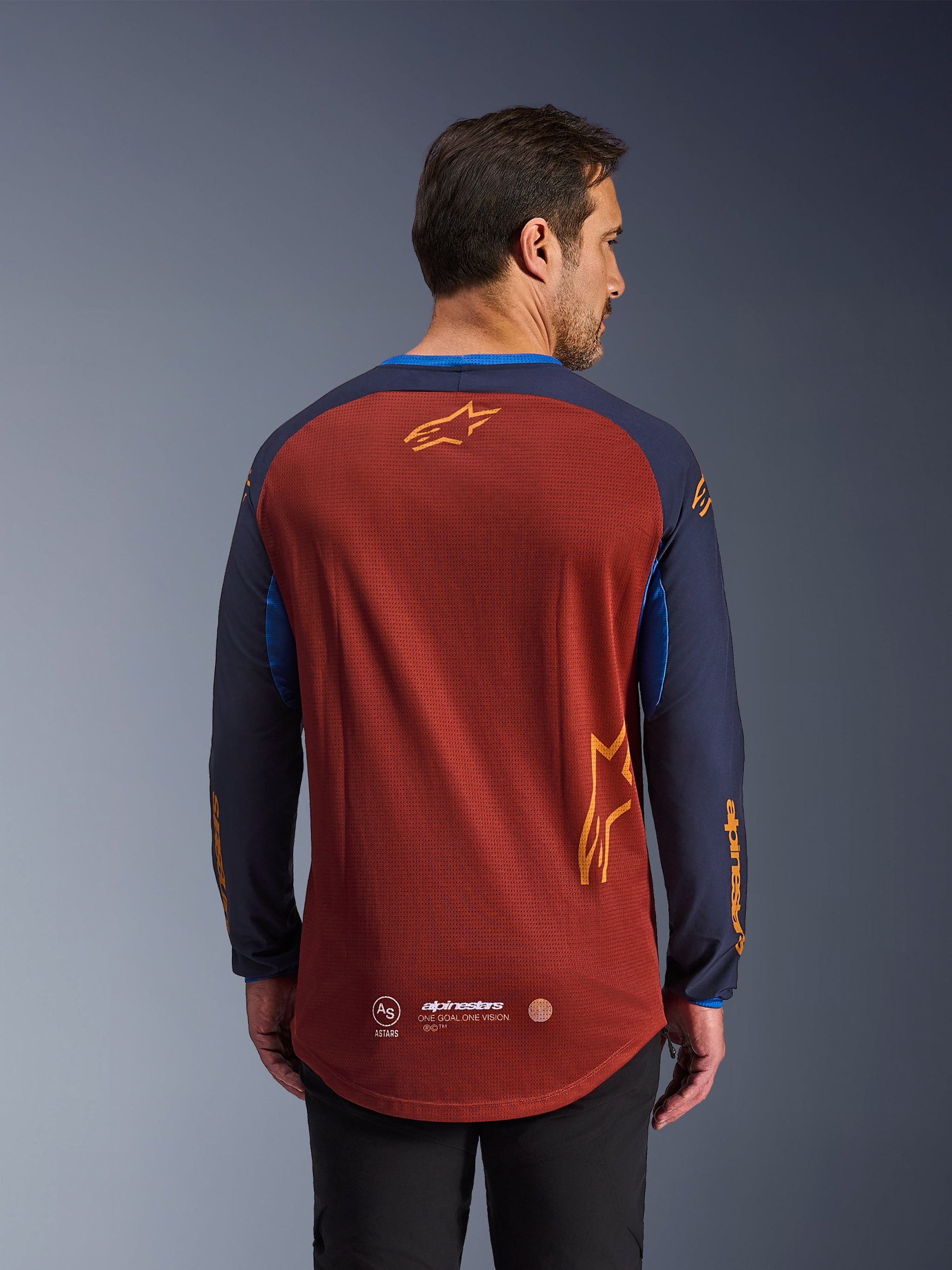 Alpinestars Maxdura Dual Jersey in Rust Brown and Mood Indigo, viewed from the back, featuring a breathable mesh torso, dark blue sleeves with orange Alpinestars branding, and a dropped rear hem for extra coverage.