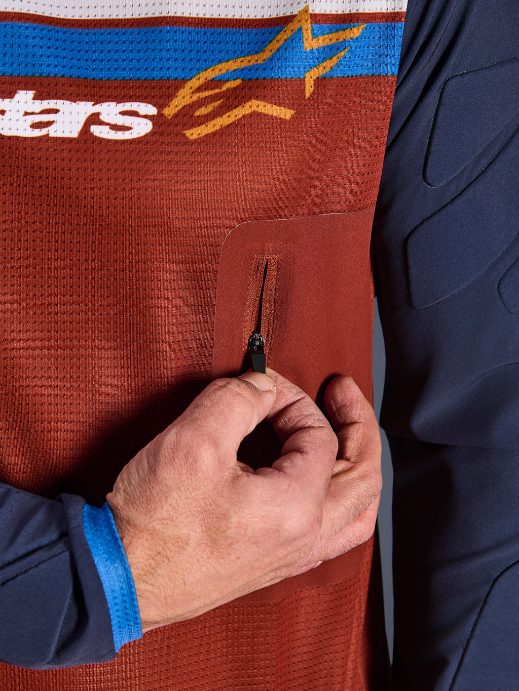Close-up van Alpinestars Maxdura Dual Jersey, roestbruine mesh torso met naadloze borstzak met ritssluiting, Mood Indigo mouwen met geïntegreerde vulling, technisch detail van adventure motorjersey