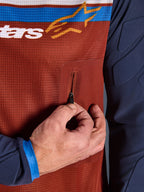 Close-up van Alpinestars Maxdura Dual Jersey, roestbruine mesh torso met naadloze borstzak met ritssluiting, Mood Indigo mouwen met geïntegreerde vulling, technisch detail van adventure motorjersey