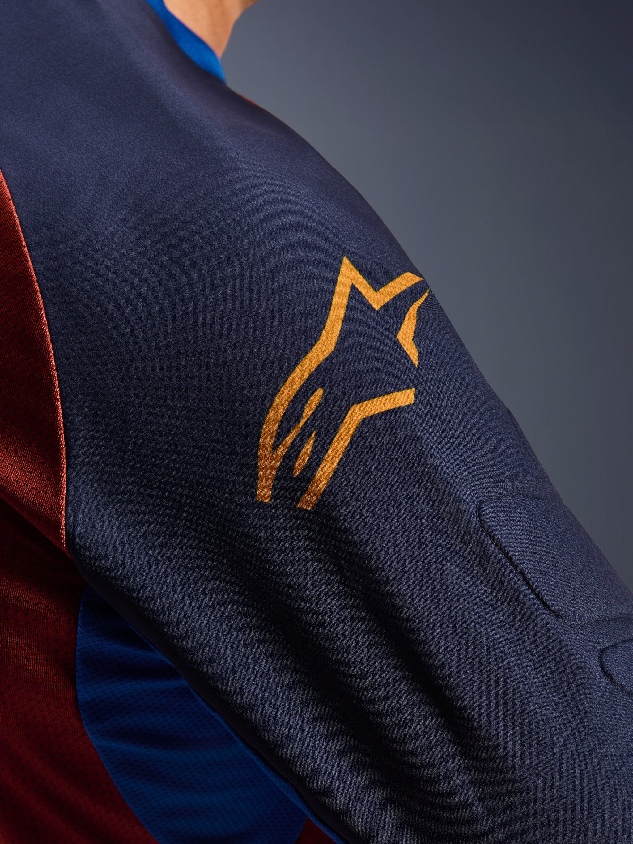 Alpinestars Maxdura Dual Jersey, close-up of the Mood Indigo sleeve with a yellow Alpinestars logo, showing integrated spacer mesh padding and Rust Brown mesh torso fabric, technical adventure motorcycle apparel