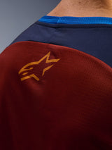 Close-up of Alpinestars Maxdura Dual Jersey, Rust Brown mesh fabric on the back, small orange star logo, dark blue upper panel and bright blue collar trim, detailed view of adventure motorcycle jersey