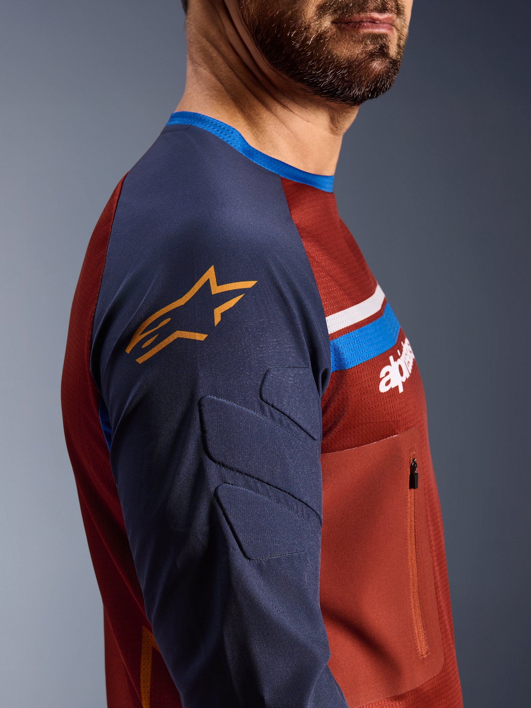Alpinestars Maxdura Dual Jersey, Rust Brown and Mood Indigo, side profile view showing padded sleeves with yellow star logo, mesh torso construction with zippered chest pocket, technical motorcycle apparel for adventure riding