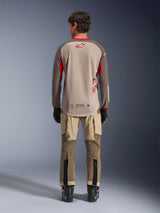 Alpinestars Maxdura Dual Jersey in Aluminum Walnut, achteraanzicht, beige mesh torso met bruine mouwen en rode logo's, verlaagde achterzoom, gecombineerd met adventure motorbroek en zwarte laarzen.