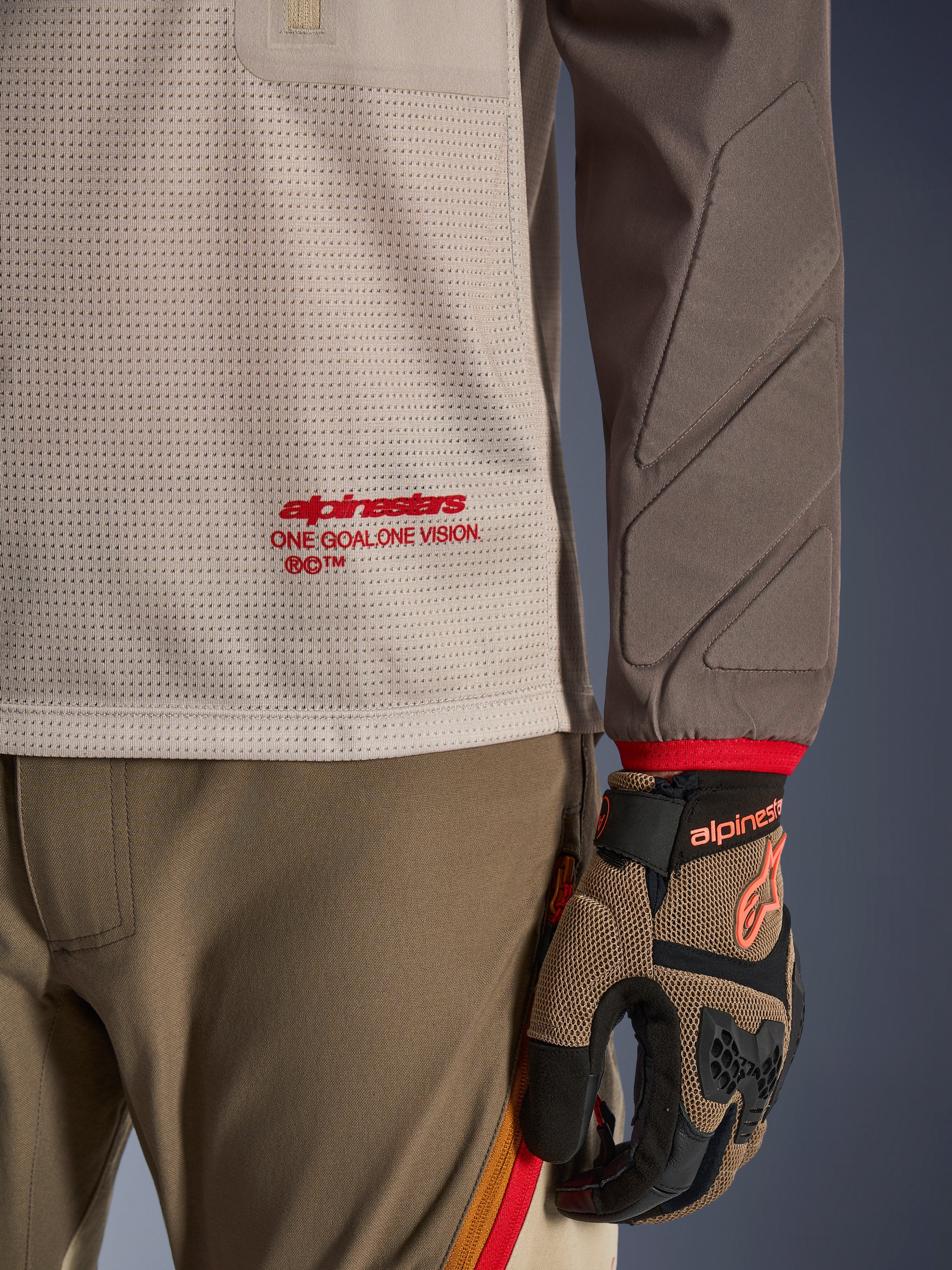 Alpinestars Maxdura Dual Jersey in Aluminum Walnut, detailweergave van de geventileerde mesh torso met rode branding, slijtvaste mouw met geïntegreerde padding, gedragen met bijpassende adventure motorbroek en handschoenen