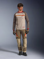 Alpinestars Maxdura Dual Jersey in Aluminum Walnut, adventure motorjersey met zandkleurige mesh torso en bruine mouwen, rode kraag en horizontale borststreep met Alpinestars-logo, gedragen met bijpassende adventure broek en handschoenen.