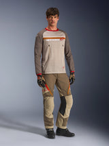 Model draagt de Alpinestars Maxdura Dual Jersey in Aluminum Walnut, voorzien van een grijze mesh torso, bruine mouwen met rode boorden en borstzakken met ritssluiting, gecombineerd met bijpassende off-road uitrusting voor adventure-rijden.