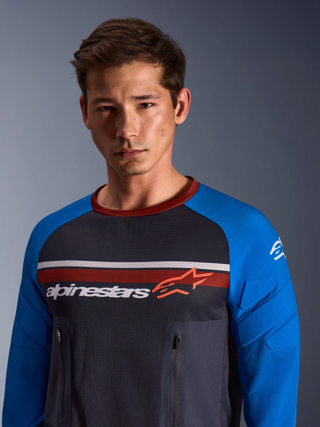Alpinestars Maxdura Dual Jersey, motorjersey, diepgrijs en koningsblauw, mesh torso, koningsblauwe mouwen met geïntegreerde padding, verticale borstzakken met rits, Alpinestars-logo op de borst, gedragen door een mannelijk model
