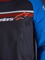 Alpinestars Maxdura Dual Jersey, detailopname van borst en mouw, donkergrijs en koningsblauw, voorzien van een borstzak met ritssluiting, ademende mesh torso en geïntegreerde padding op de mouwen, met het Alpinestars-logo over rode en witte strepen.